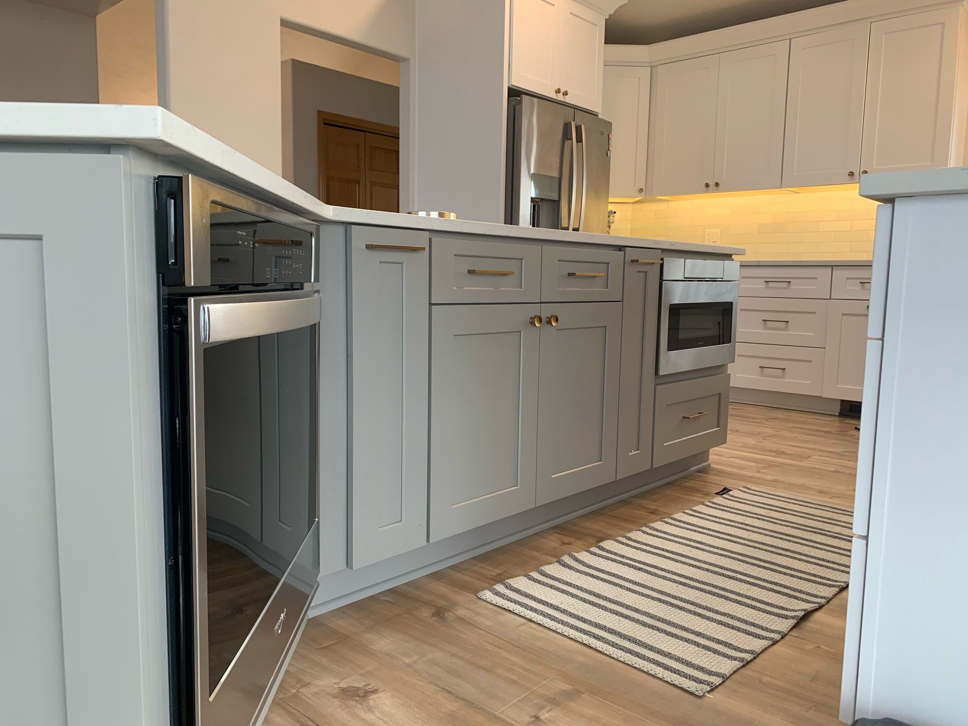 Kitchen with gray cabinets, stainless steel appliances, and a striped rug on wooden floors.