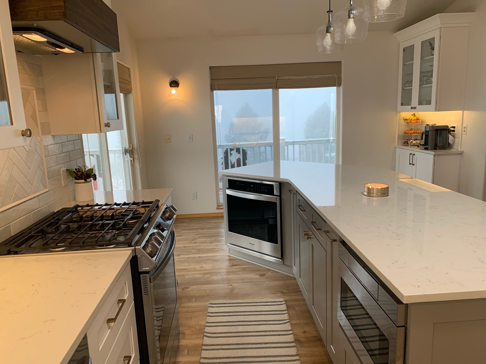 Modern kitchen with stove, island, oven, and view of snowy outdoors.