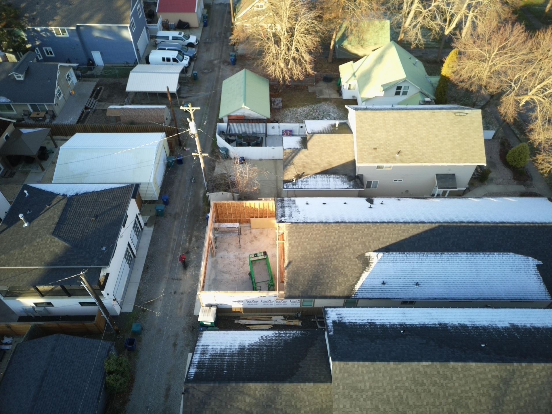 Aerial view of a street with houses and a newly framed construction. Some snow is visible on the roofs.