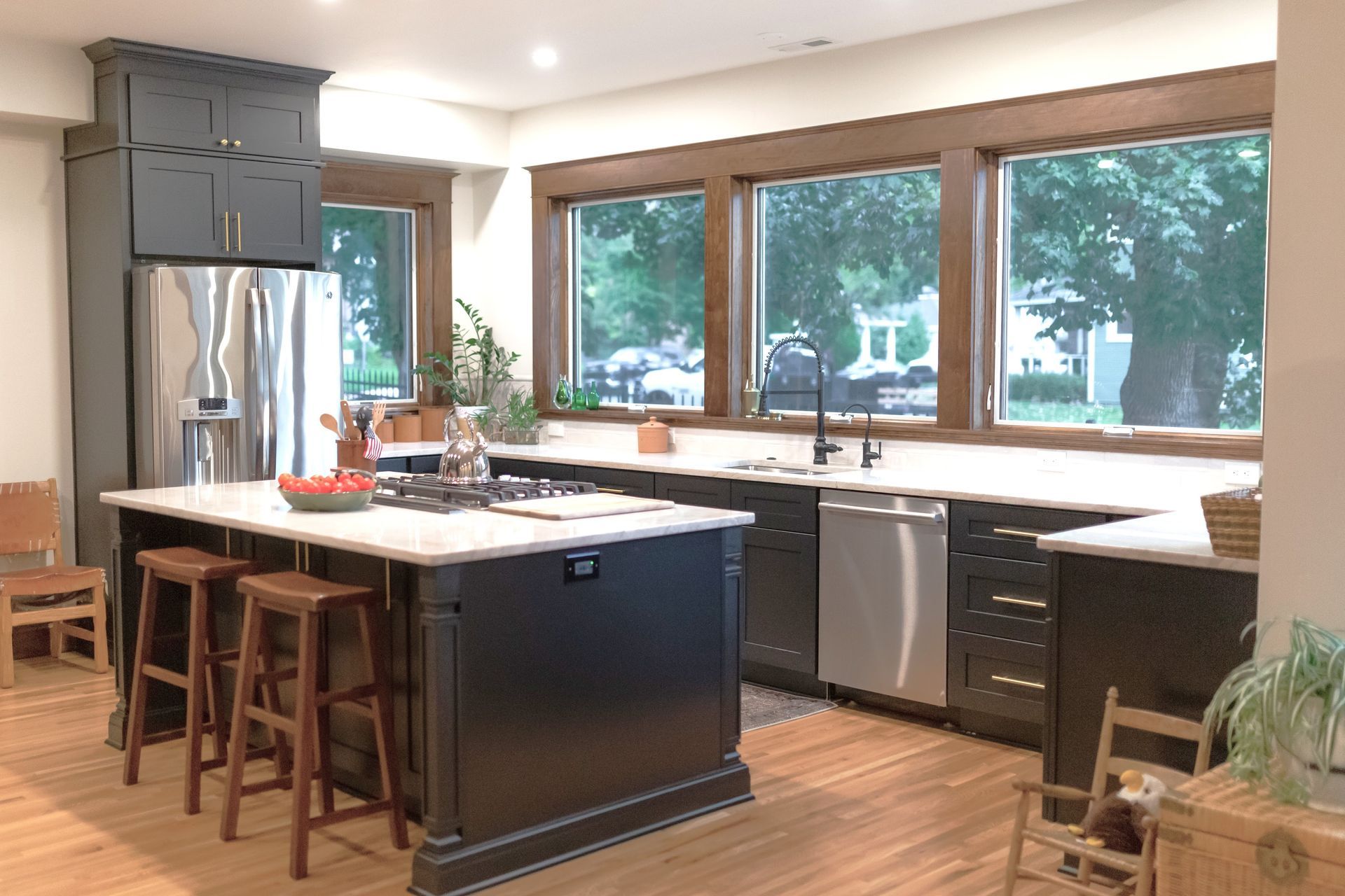Modern kitchen with dark gray cabinets, light counters, stainless steel appliances, and wood floors.