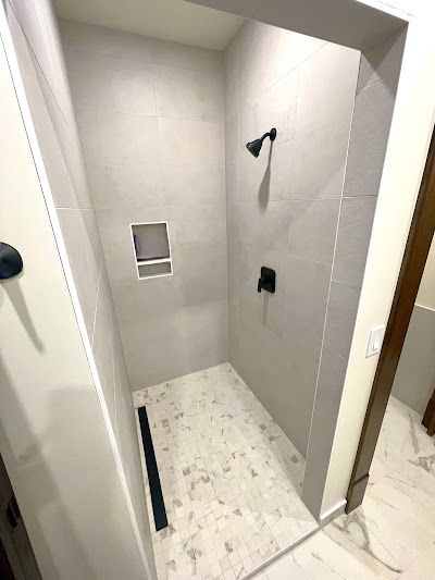 A modern walk-in shower with gray tile walls, black fixtures, and light marble flooring.