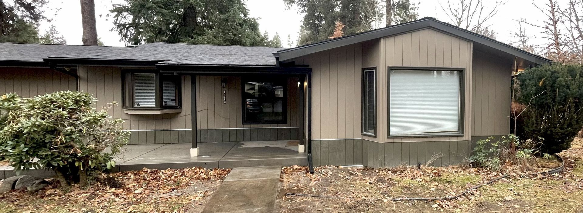 A tan, single-story house with a porch. Trees and a sidewalk are in front.