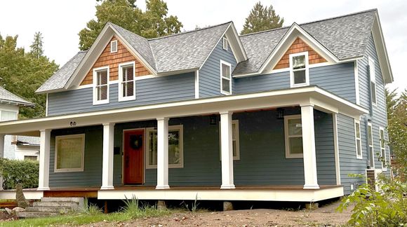 Blue two-story house with a porch, columns, and a gabled roof. Brown trim and red door.