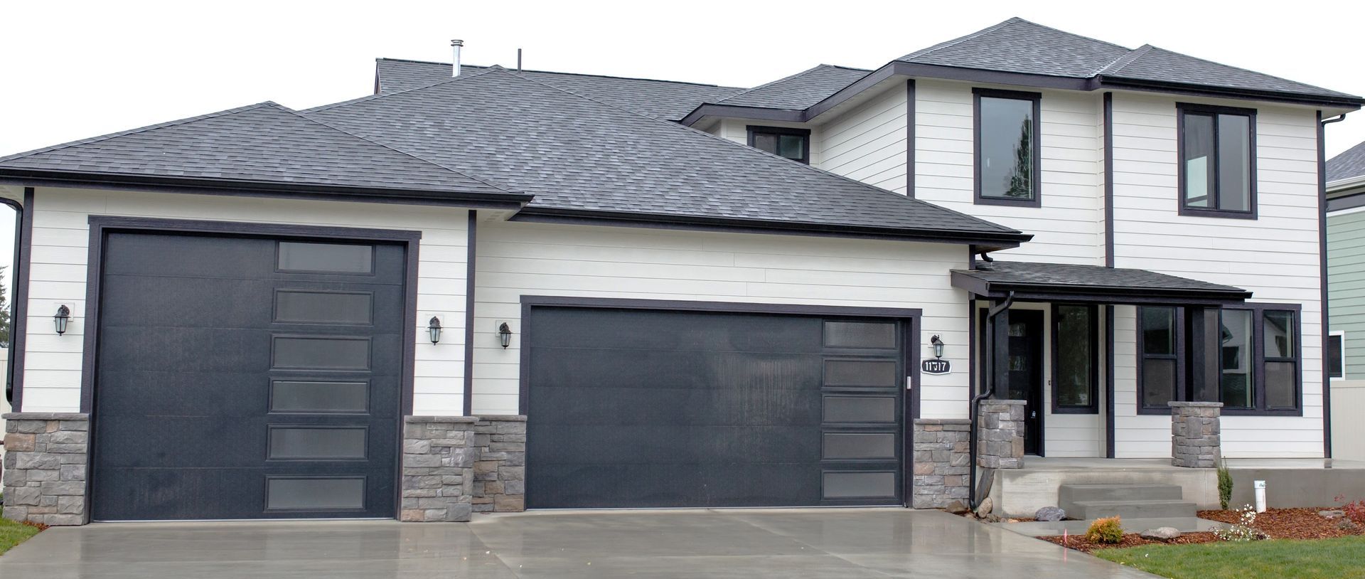 Modern white house with black trim, garage doors, and roof. Stone accents on the facade.