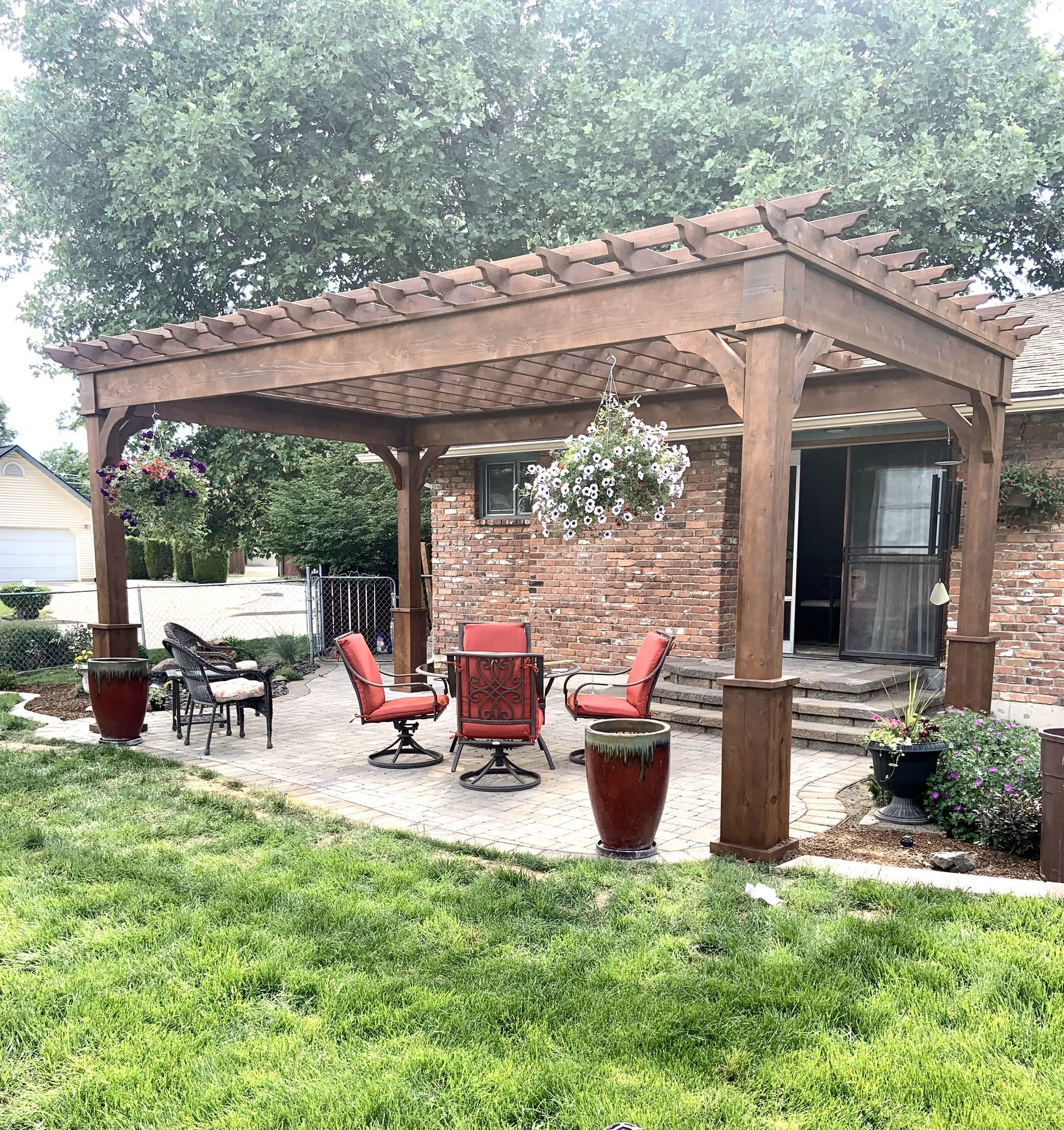 Pergola over patio with red chairs, brown pots, and hanging flowers.