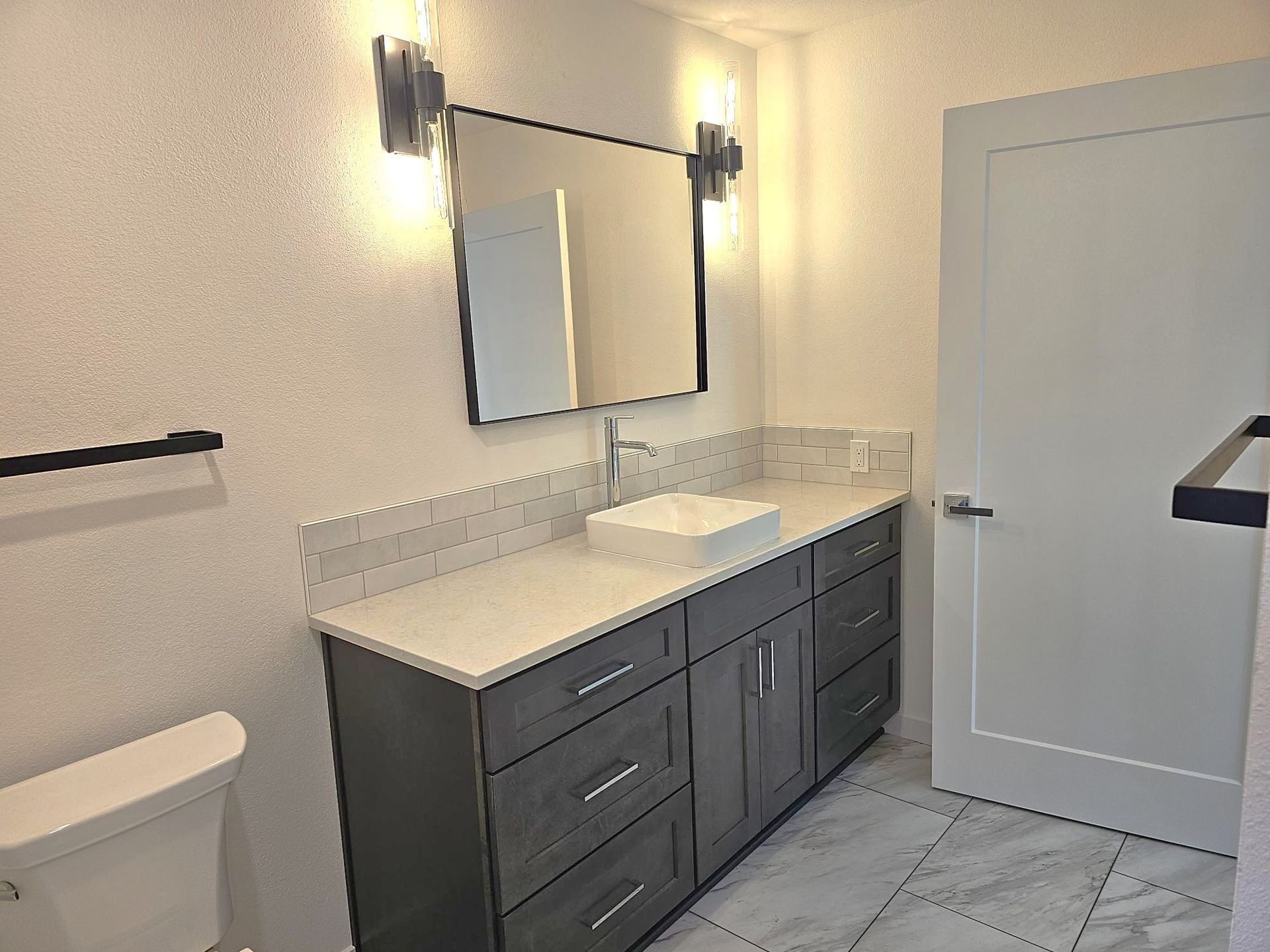 Modern bathroom with dark gray vanity, white countertop, and large mirror.