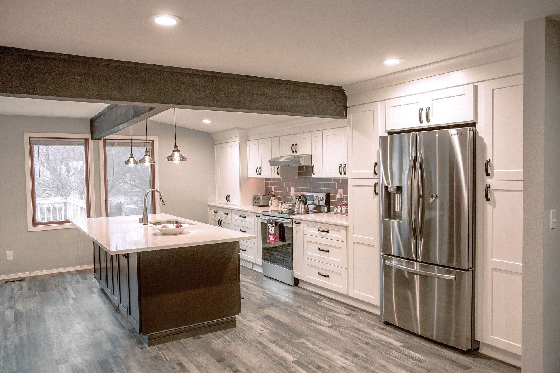 Modern kitchen with white cabinets, stainless steel fridge, and dark island, gray flooring.