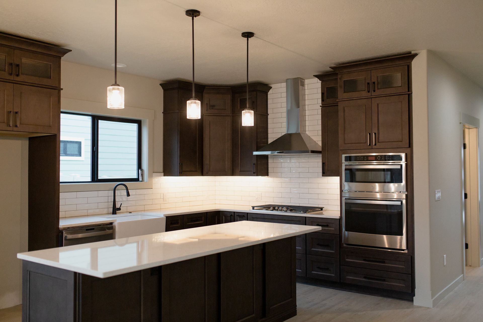 Dark brown kitchen with white countertops, stainless steel appliances, and pendant lights.