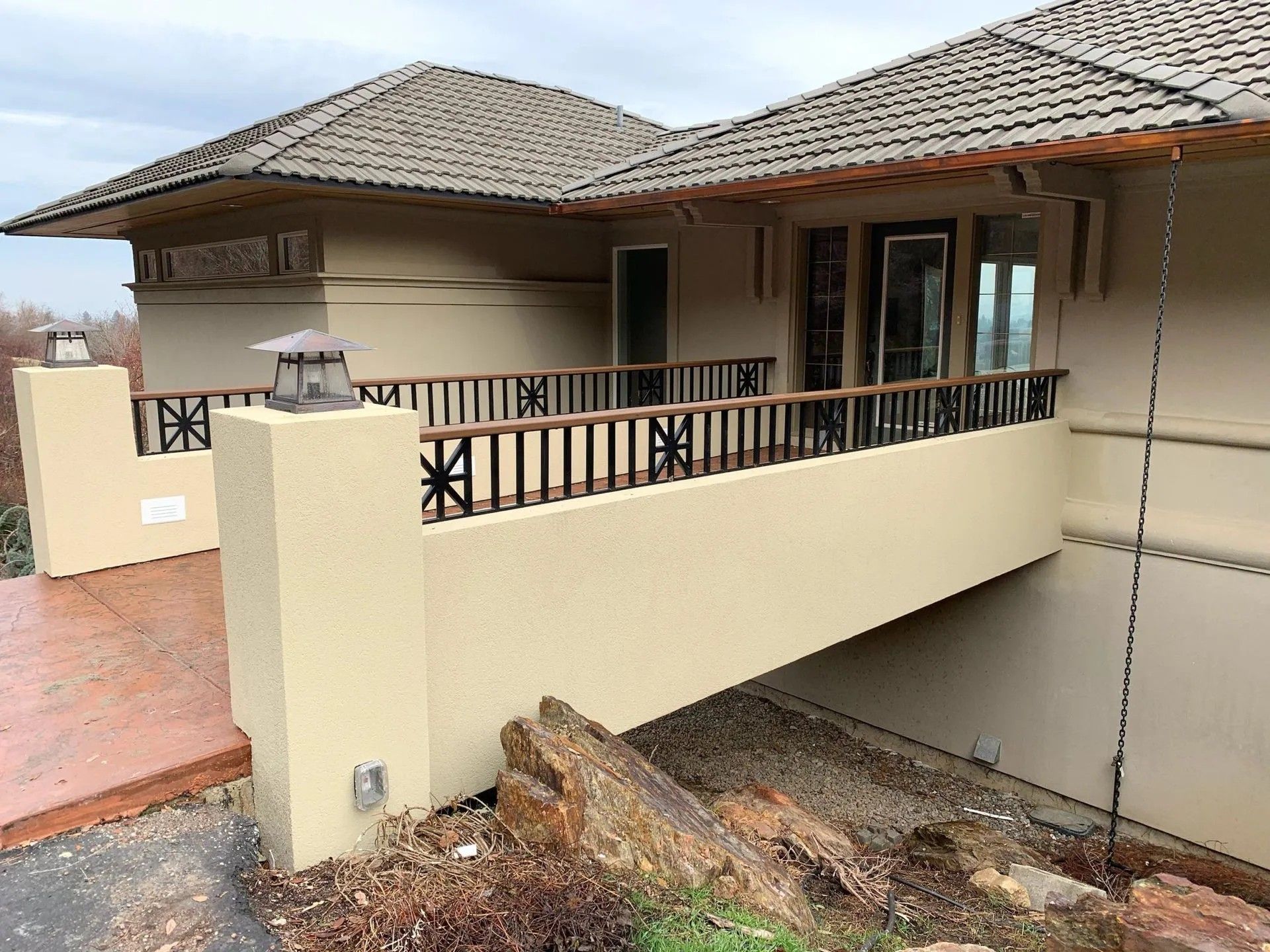 Tan house with brown roof, railing, and a porch bridge. Exterior with overcast sky.