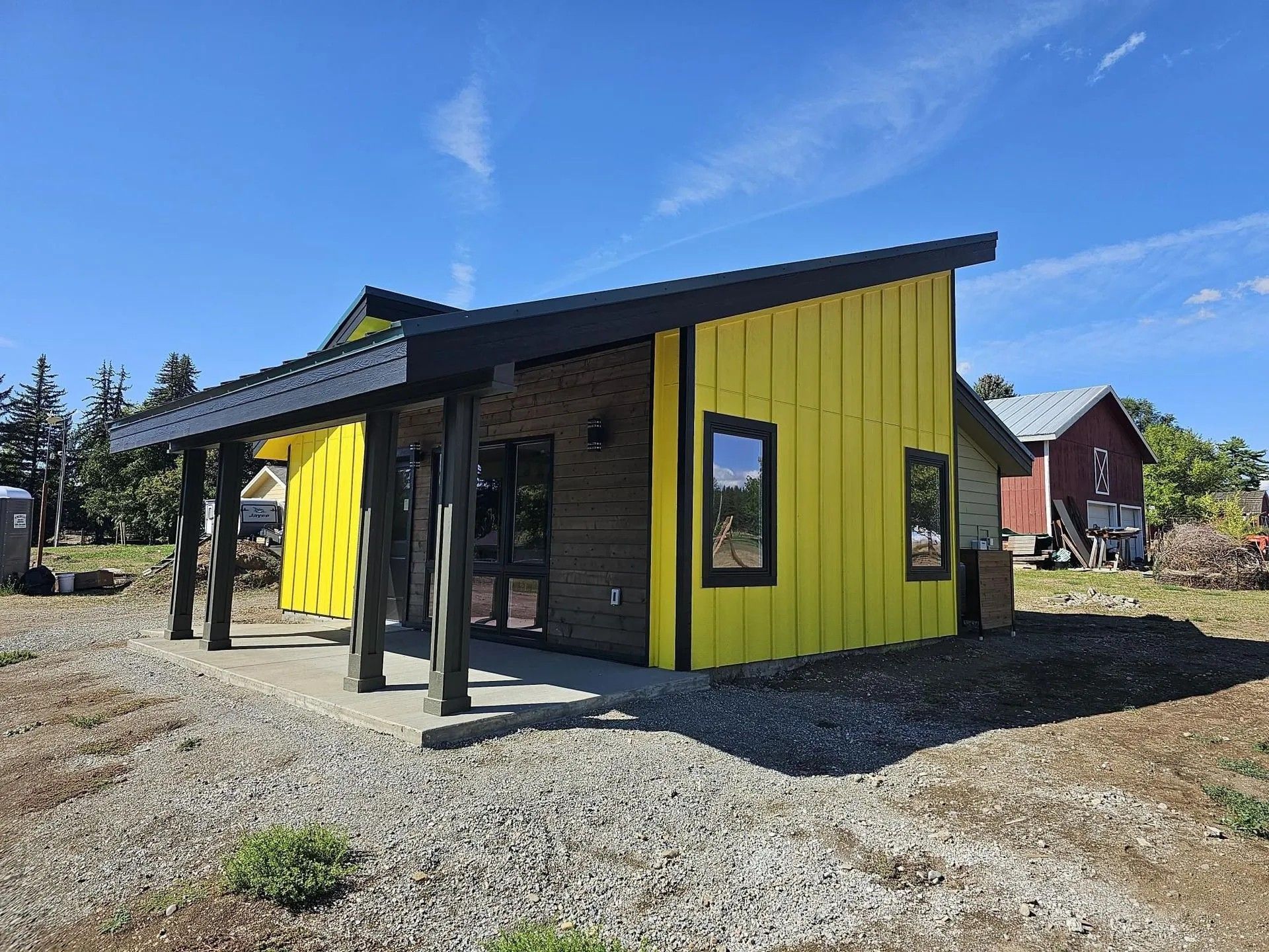 Yellow and brown modern building with a covered entrance, on a gravel lot under a blue sky.
