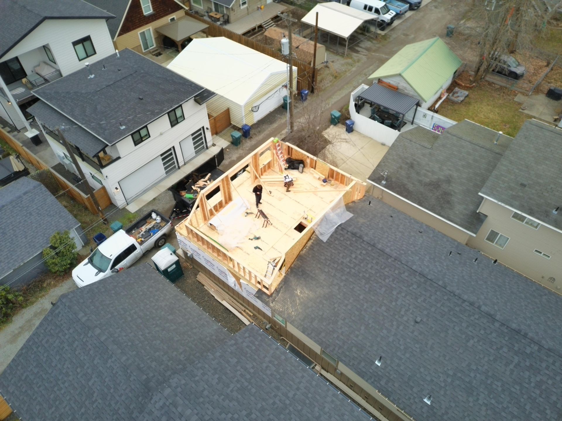 Aerial view of a wood-framed building under construction with workers. Houses surround the construction site.