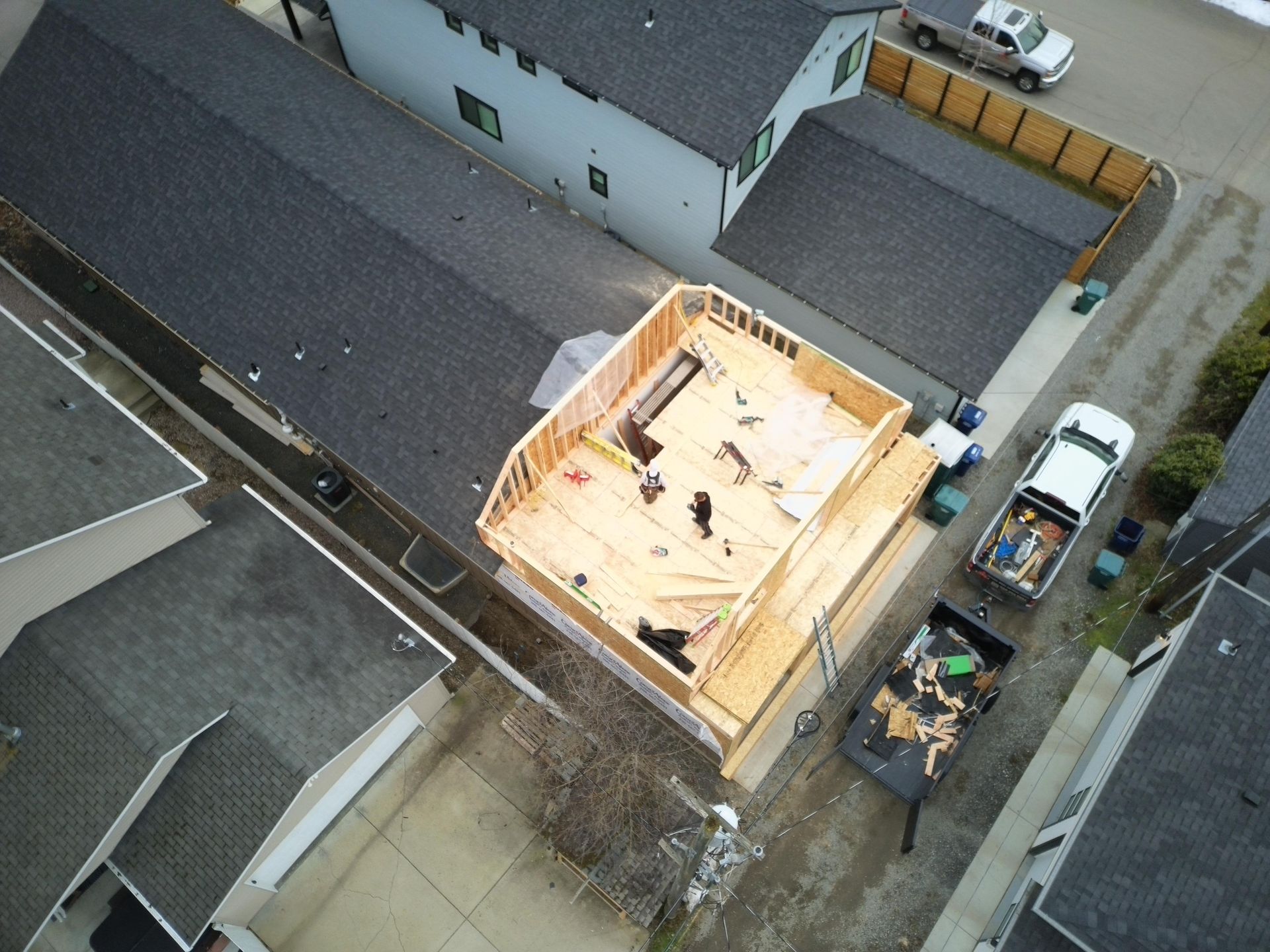 Aerial view of a home addition under construction; wooden frame, materials, and workers visible.