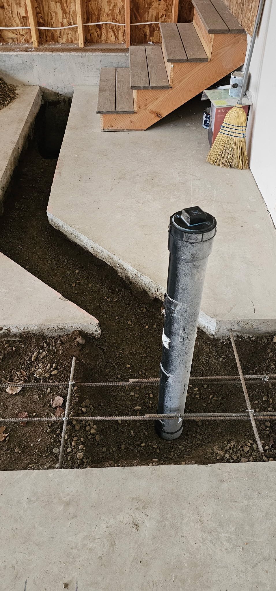 Construction site with a buried pipe. Rebar grid in the trench. A partially constructed stairway is in the background.