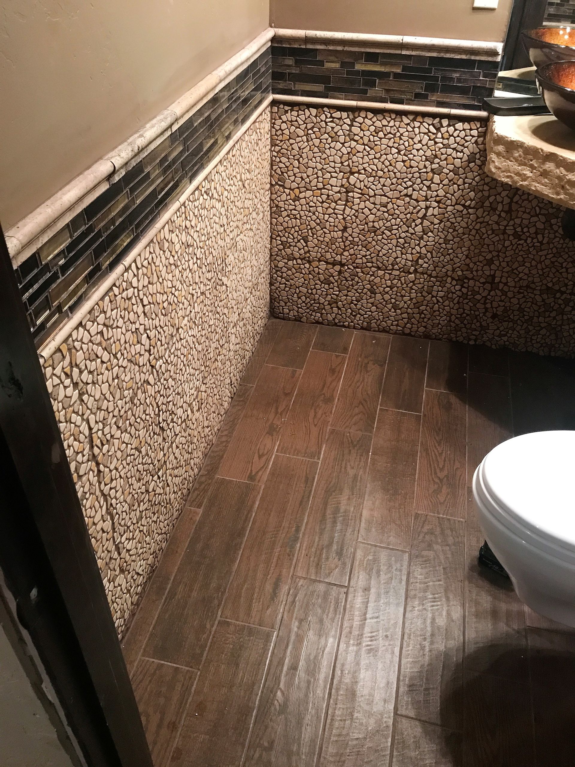 Small bathroom with textured stone walls and wood-look flooring.