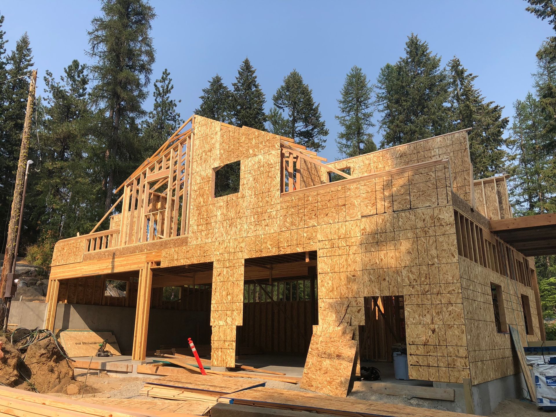 Two-story house under construction, framed with wood, set against a background of trees and clear sky.