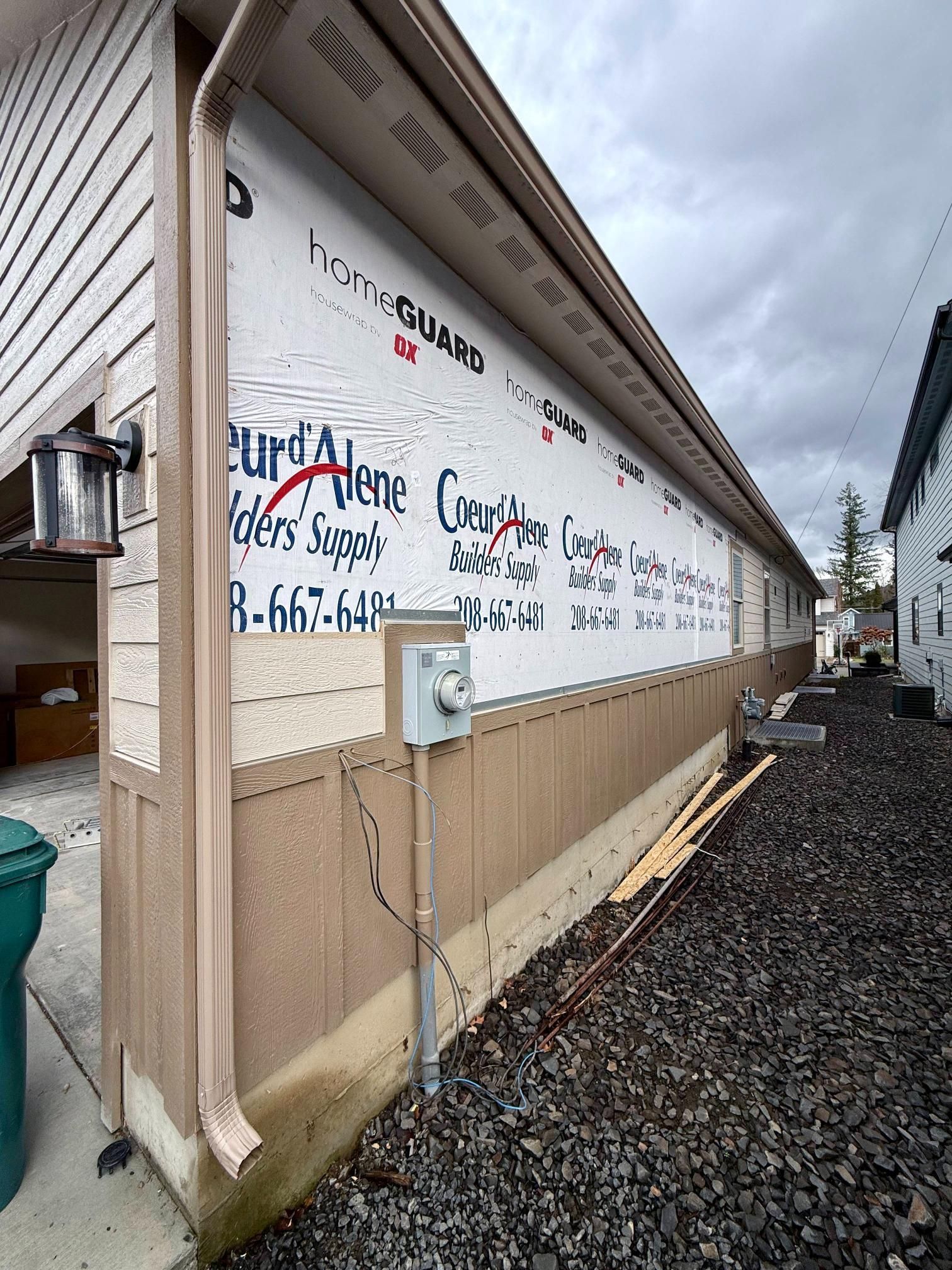 Exterior wall under construction with white protective wrap and tan siding.
