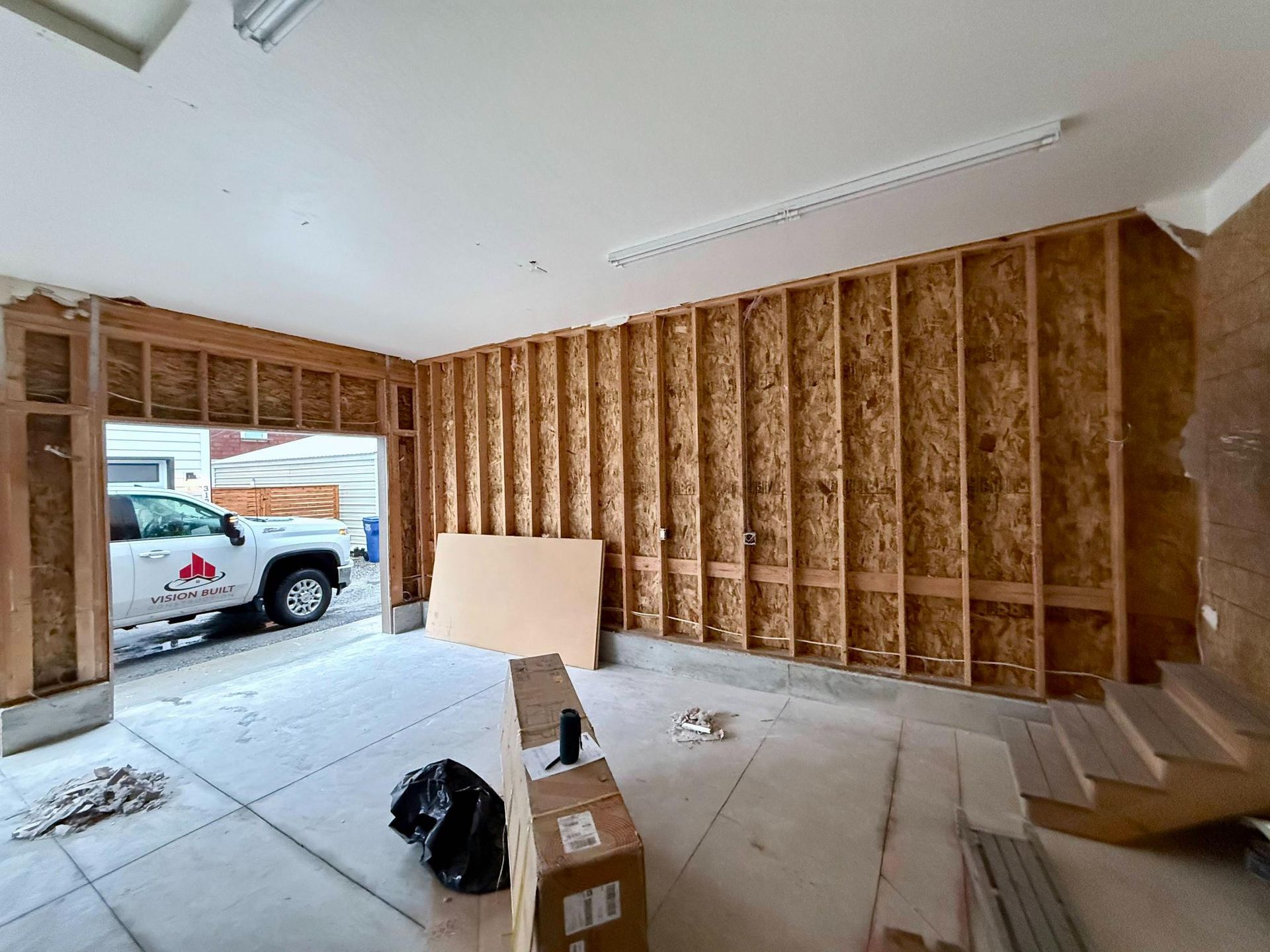 Garage interior with exposed wooden studs, open garage door, truck visible.
