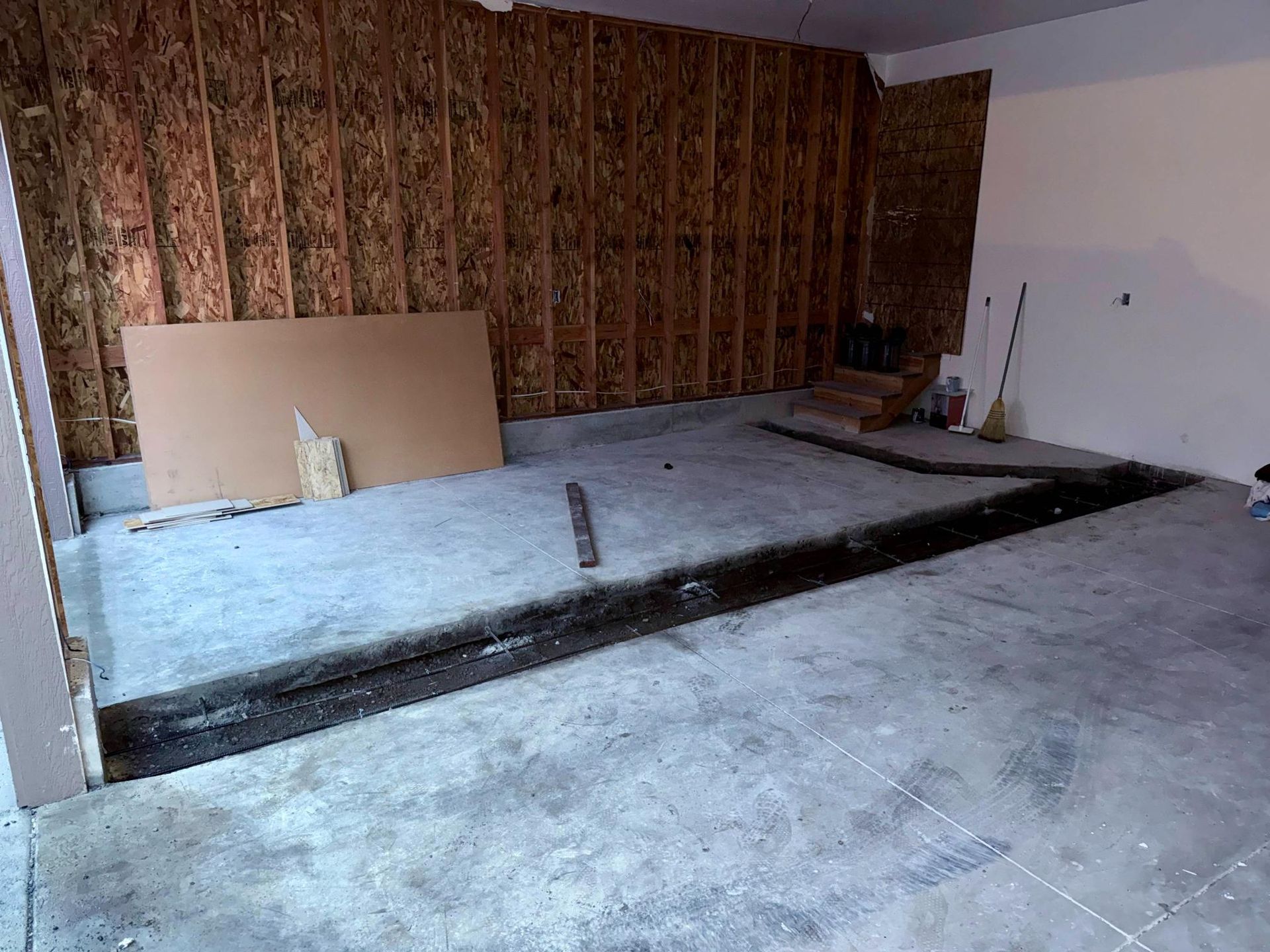 Garage interior with unfinished OSB walls and concrete floor. A long, dark trench is cut into the floor.