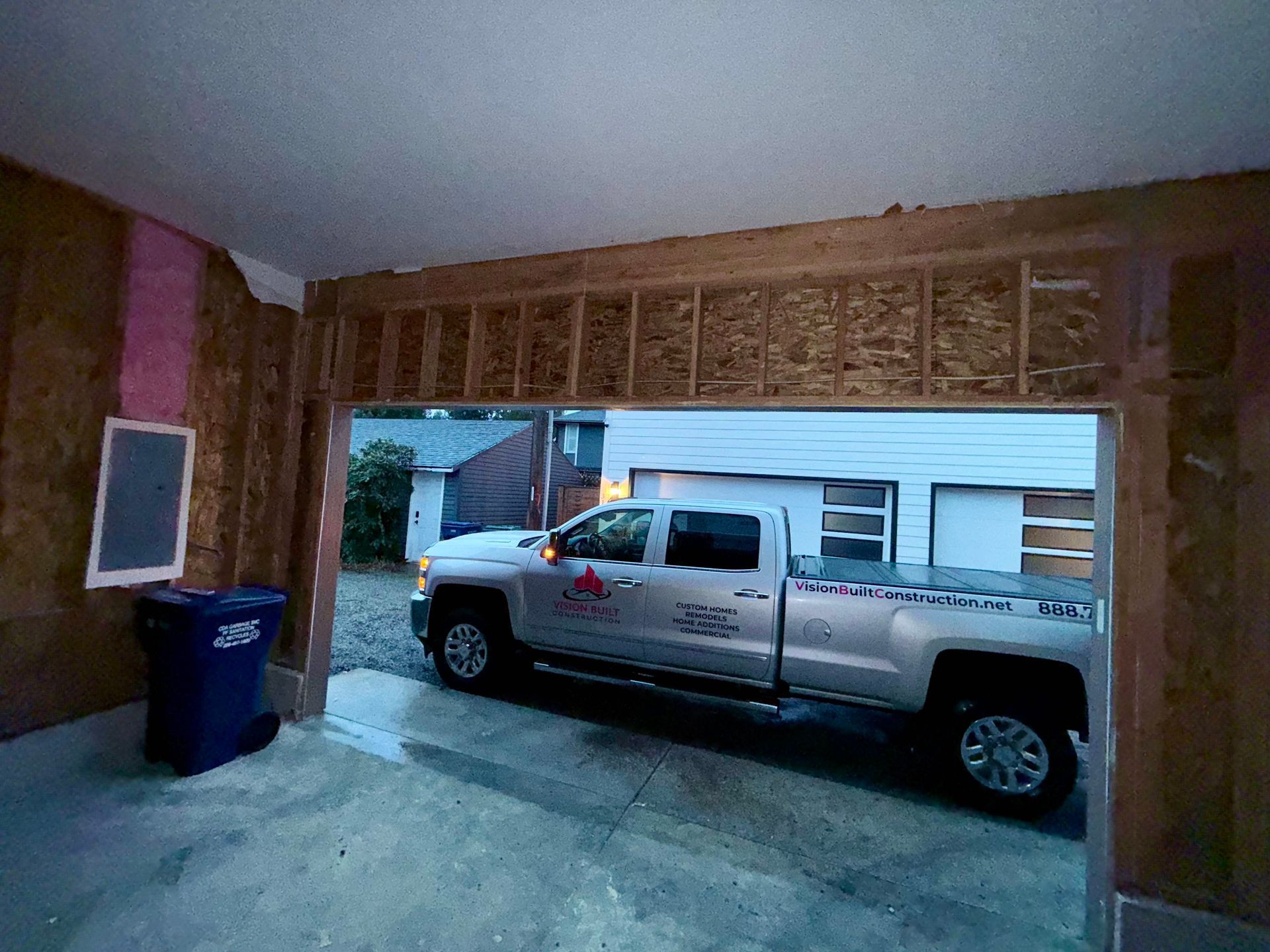 Silver pickup truck parked inside a garage opening, viewed from within. Garage is under construction.