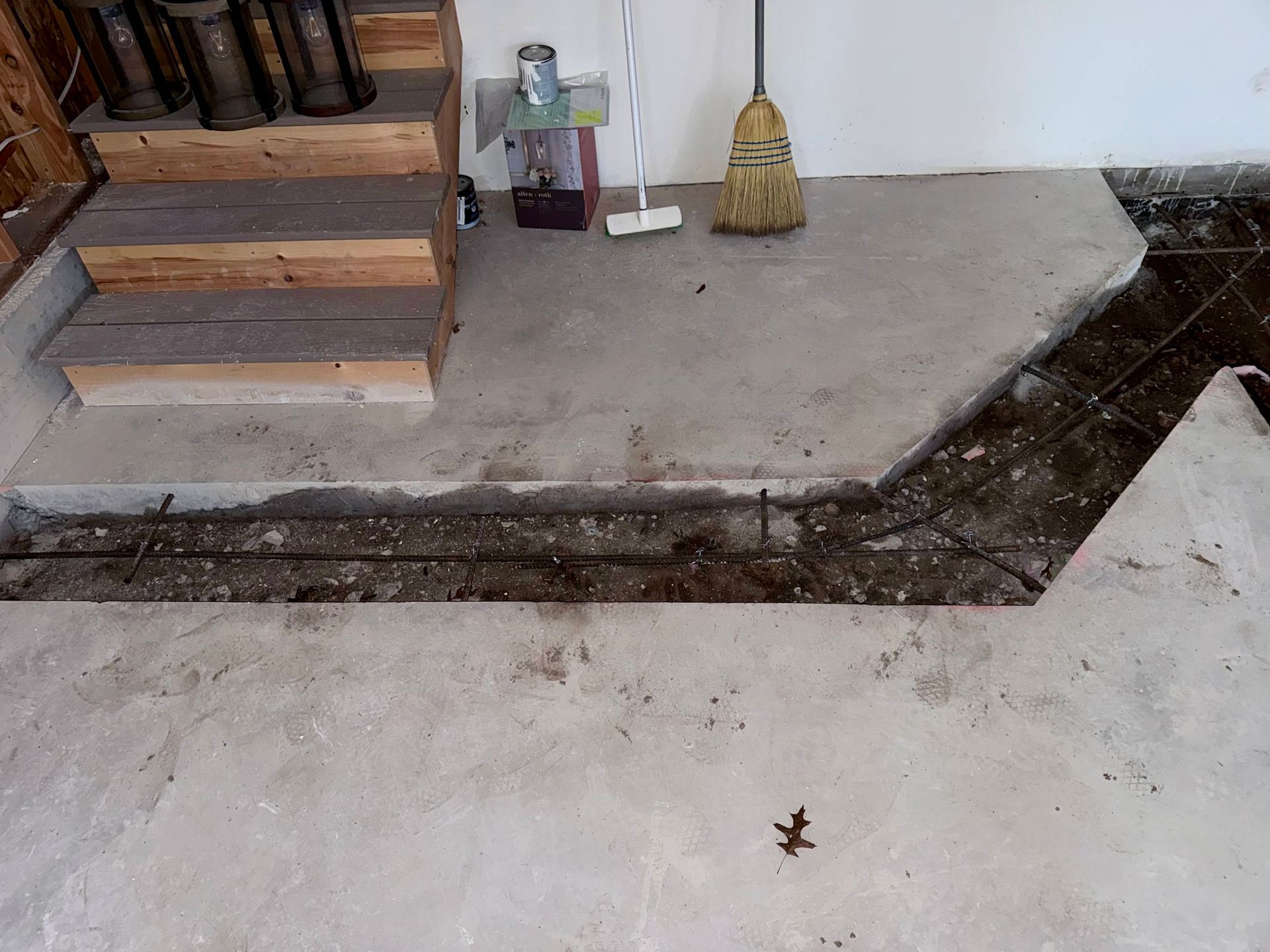 Concrete floor partially demolished, exposing rebar. Stairs and broom in background.
