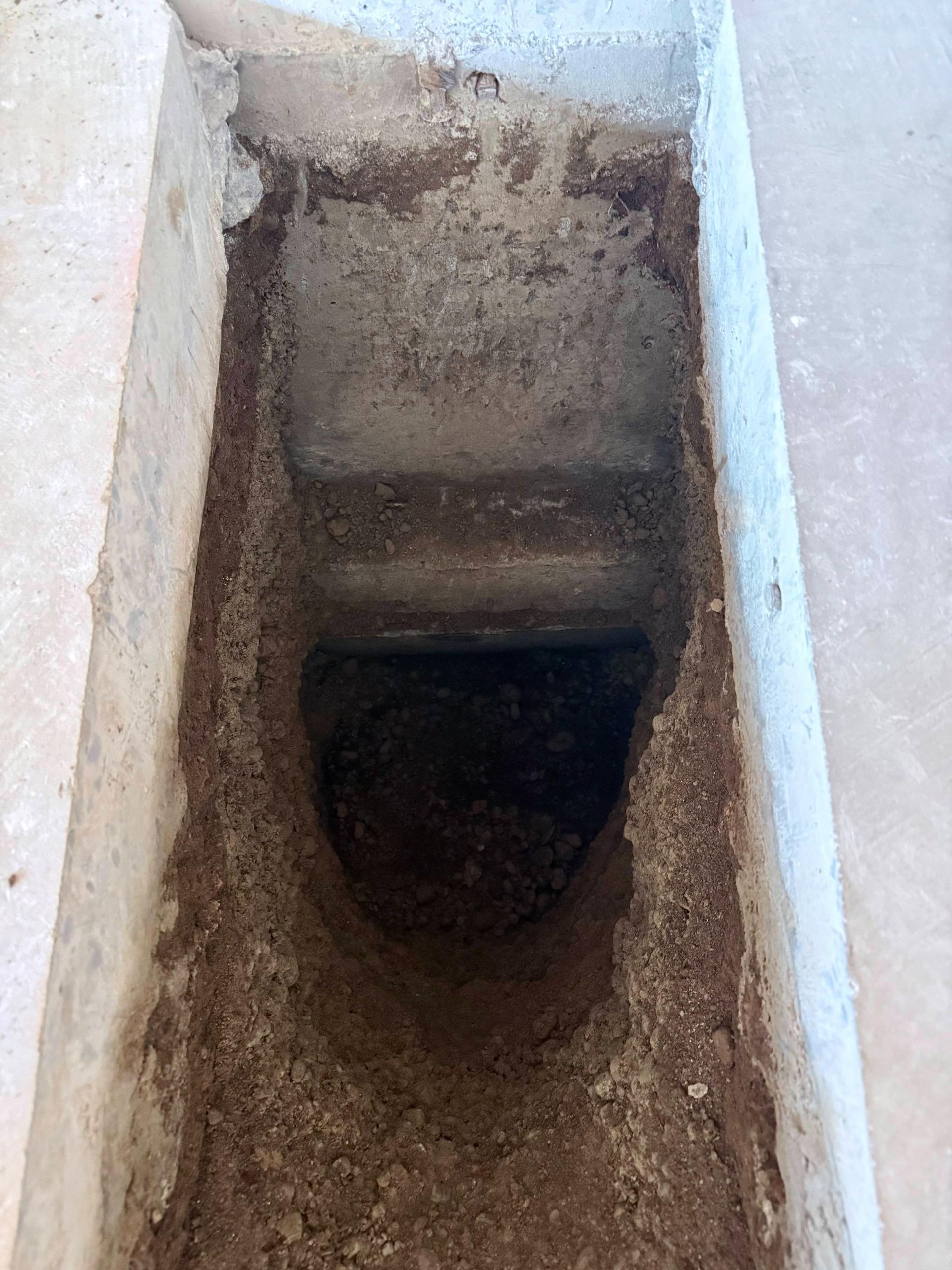 Long, narrow, earthen trench with a rectangular opening at the top, leading into a dark pit.