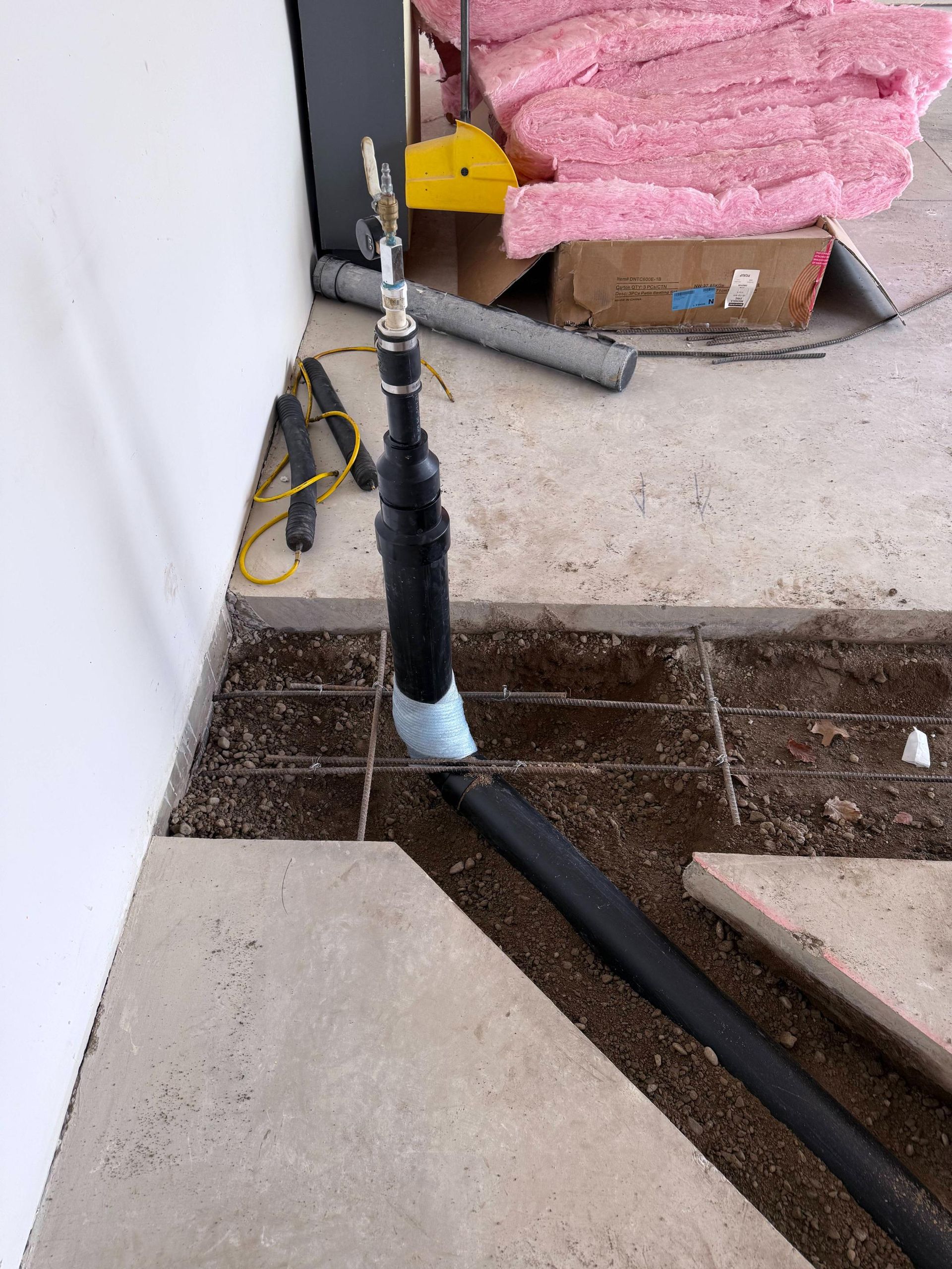 Black pipe extending from concrete floor, construction setting, insulation in background.