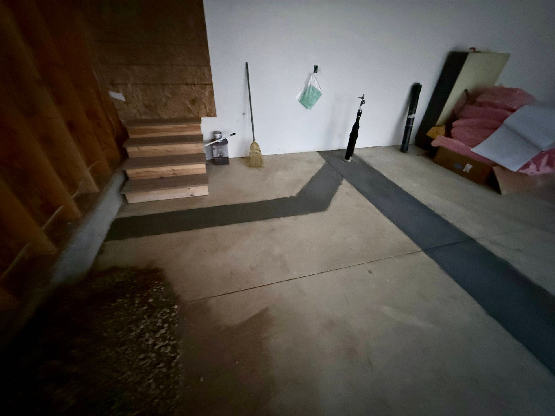 Concrete floor with a dark gray path, a small staircase, and various items stored against the walls.