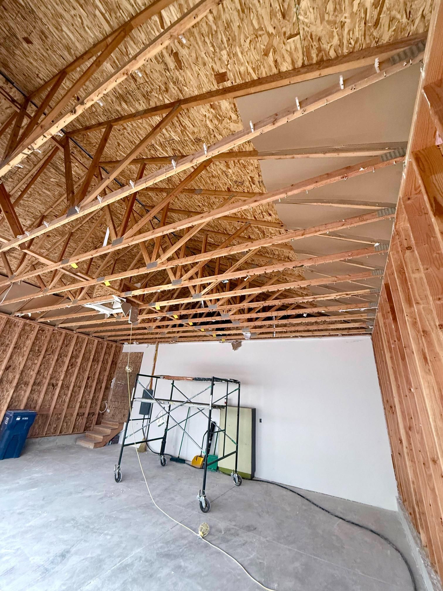 Interior view of a building under construction, showing exposed wooden trusses and partially covered ceiling.