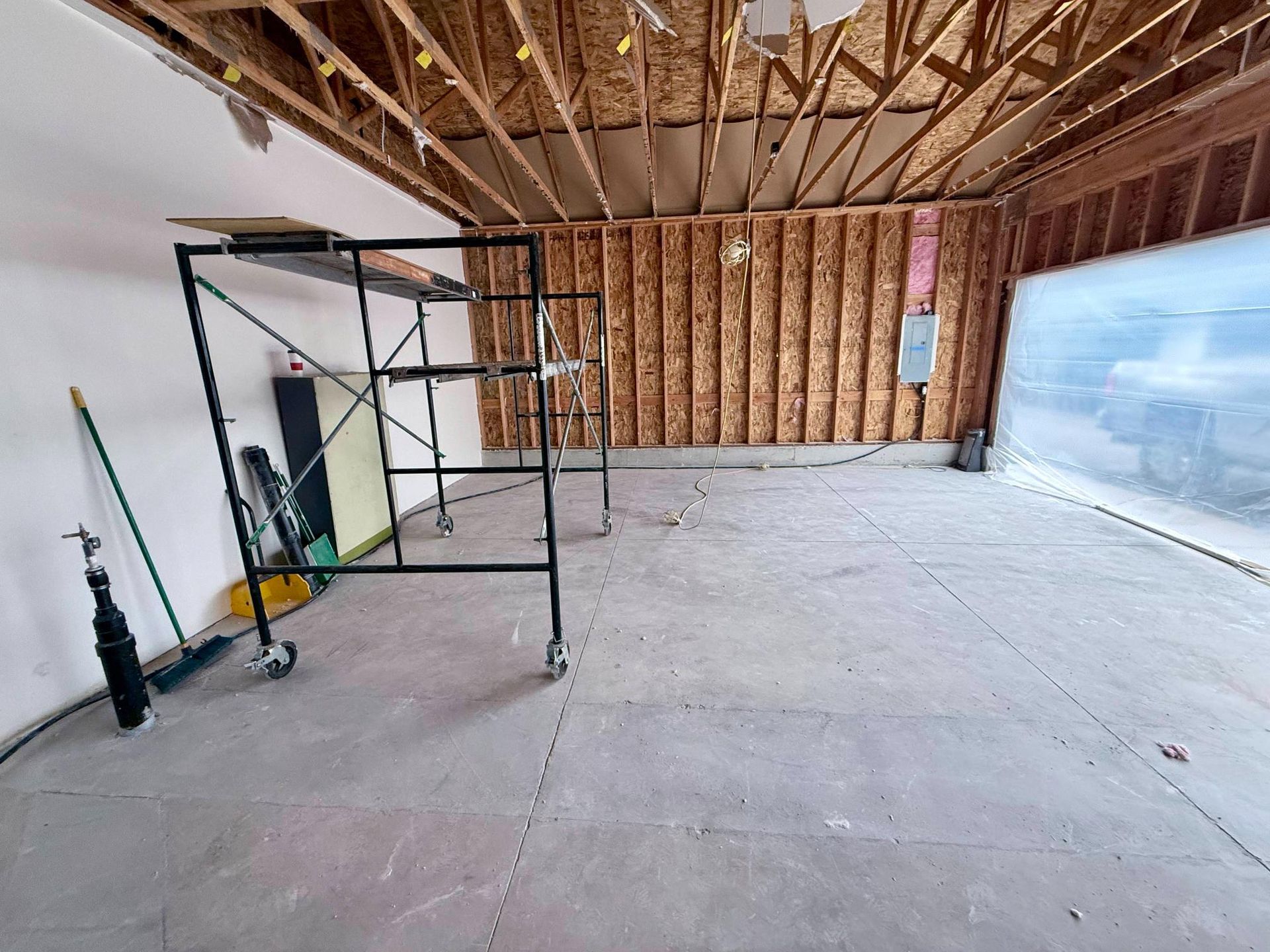 Interior of a room under construction with a concrete floor, exposed wooden beams, and scaffolding.