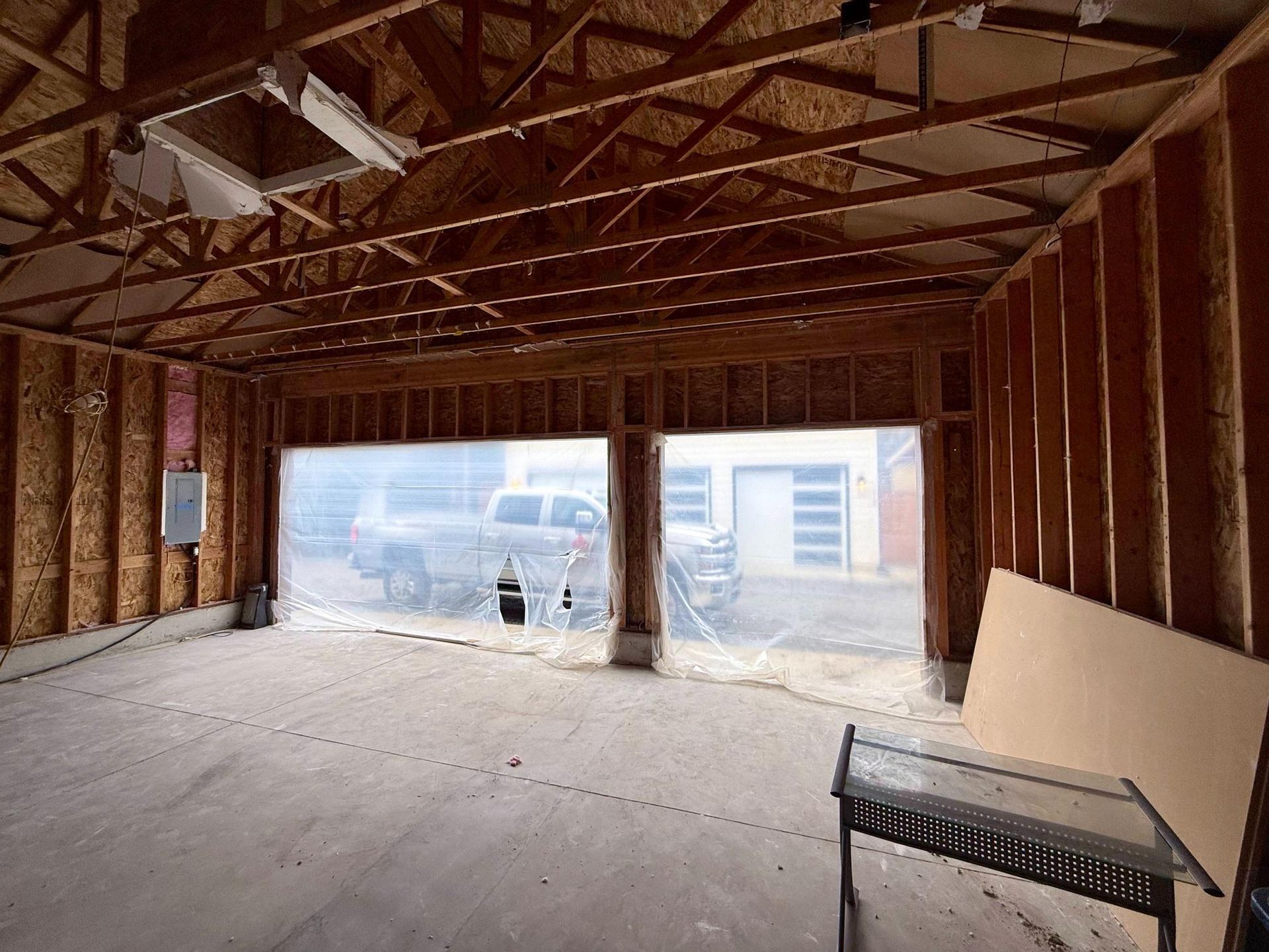 Unfinished garage interior with exposed wooden framing and two garage door openings covered with plastic sheeting.