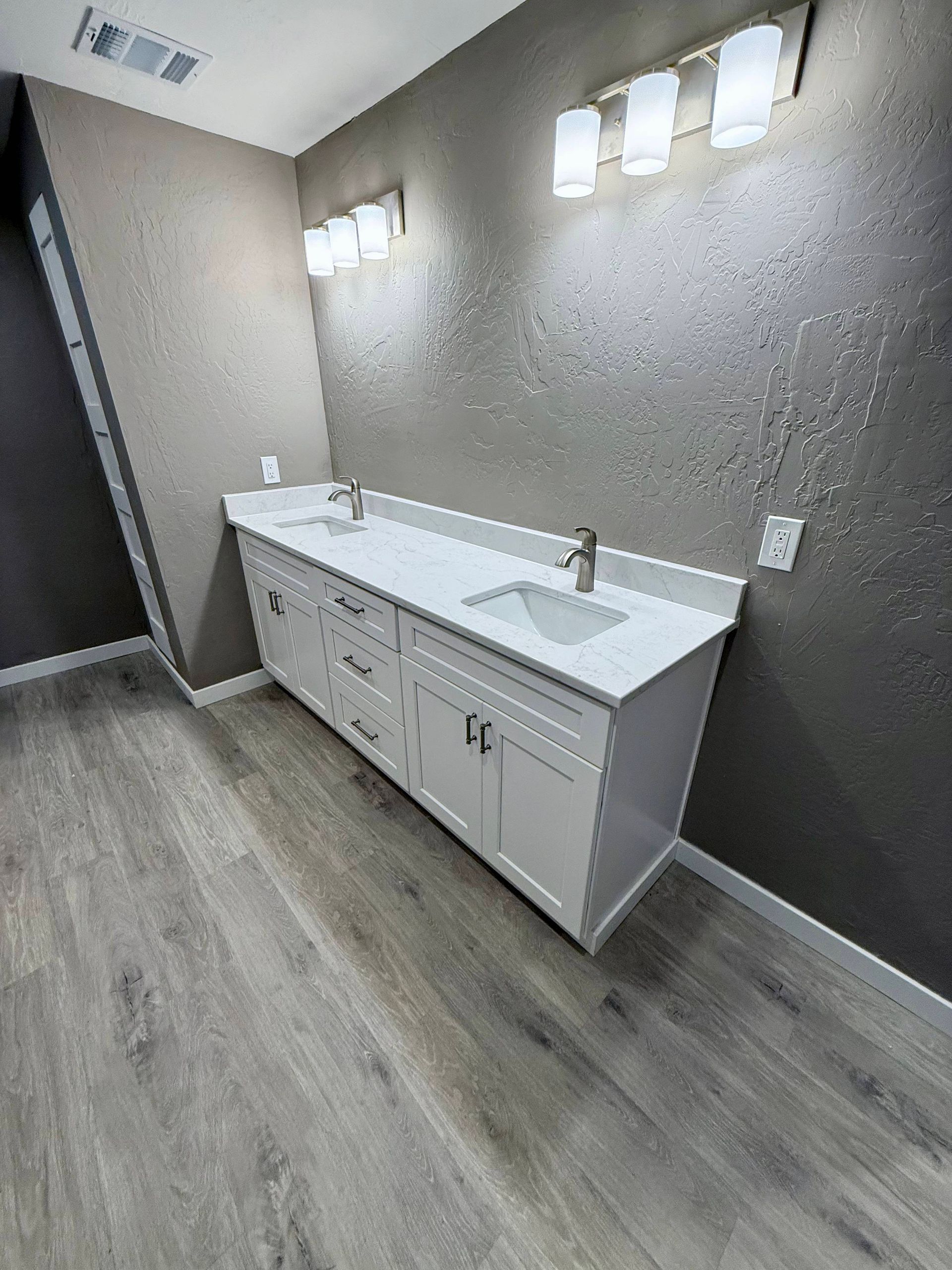 Bathroom with white double vanity, gray walls, and wood-look flooring. Two light fixtures above.