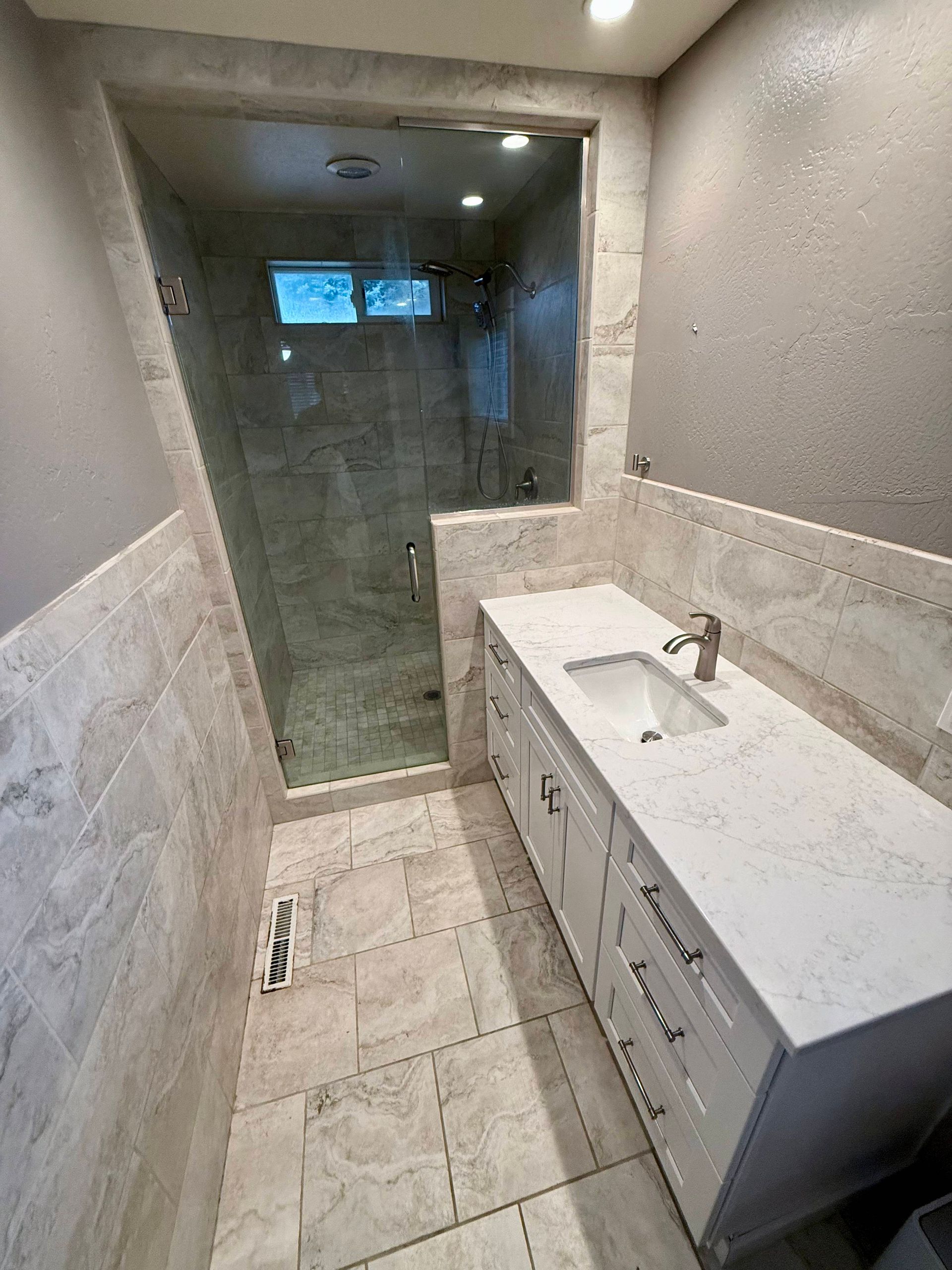 Basement with grey walls and carpet, a dark wood bar with cabinets, and recessed ceiling lights.