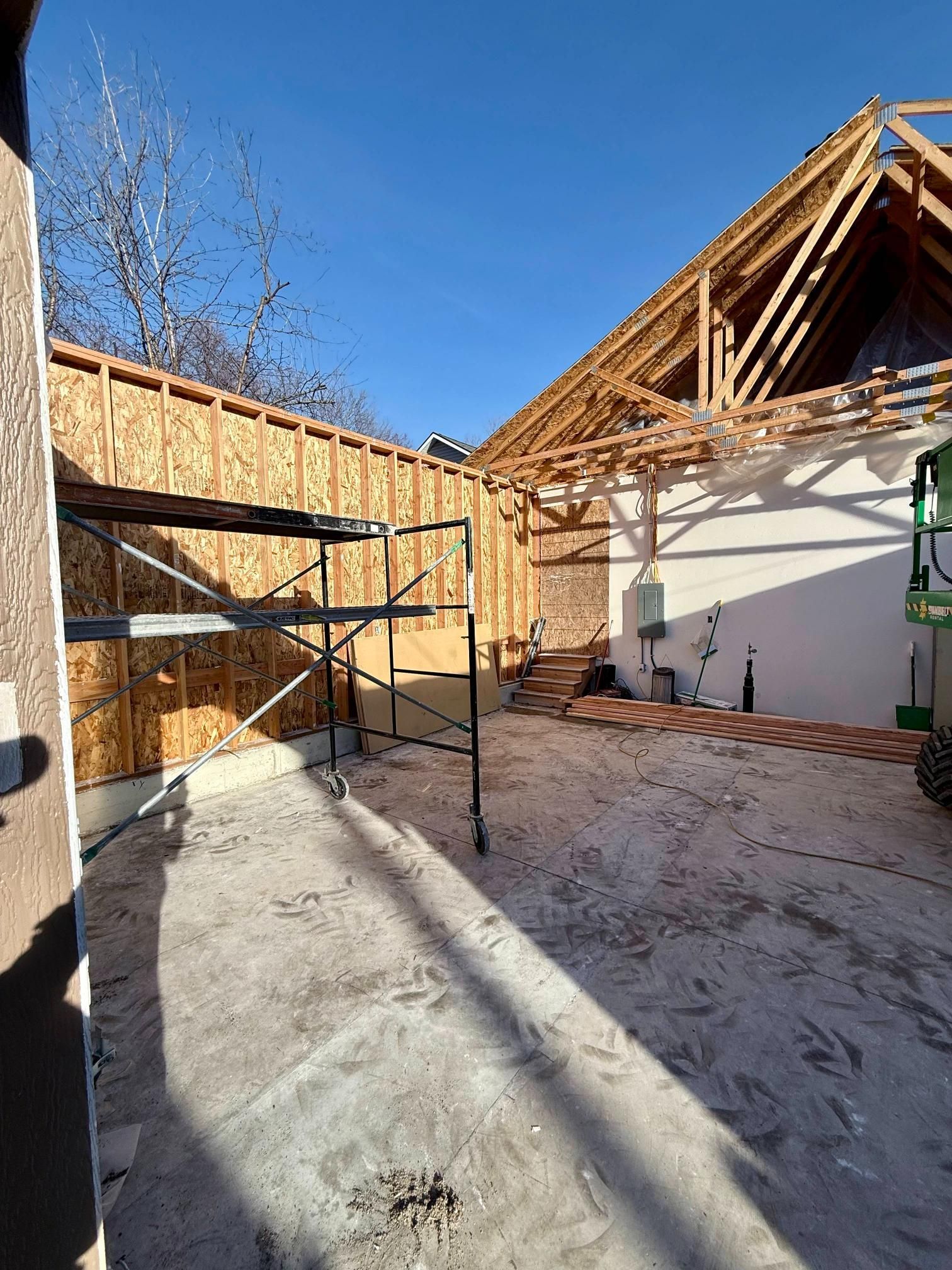 Construction site: wooden roof frame, unfinished walls, scaffolding, bright blue sky.