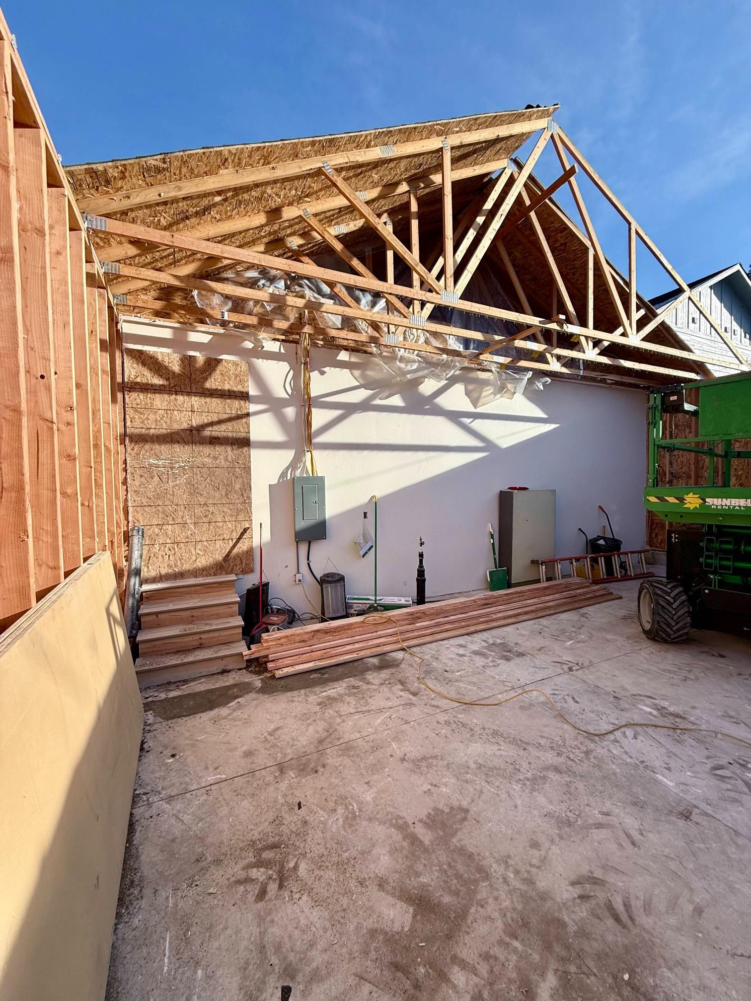 Construction site with wooden framing, exposed wall, and roofing beams under a blue sky.