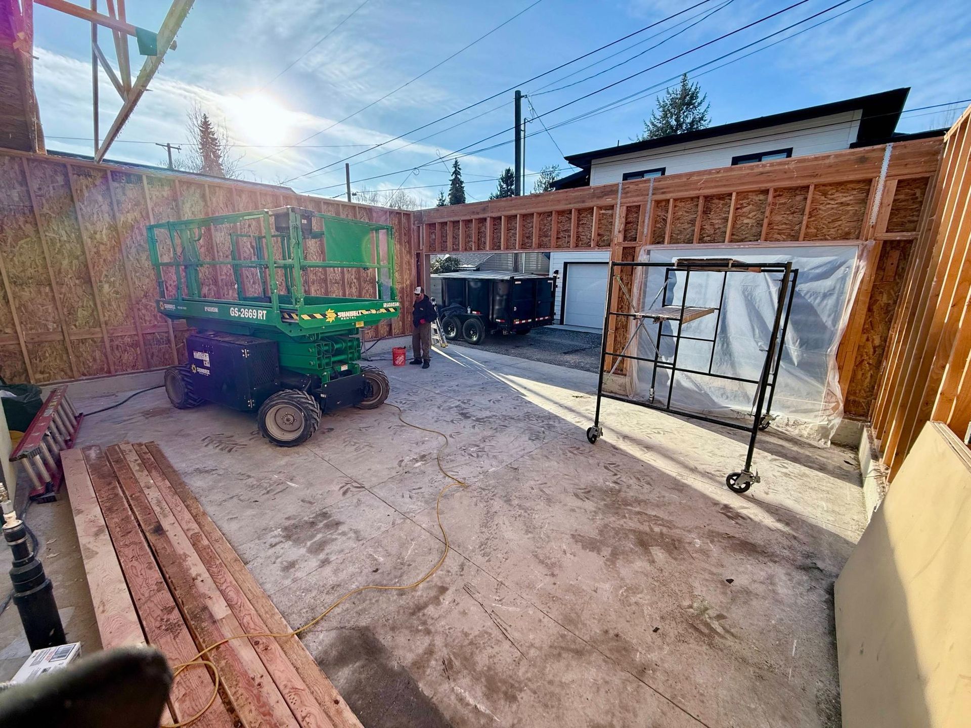 Construction site with a green lift, wooden framing, and a partially built garage.