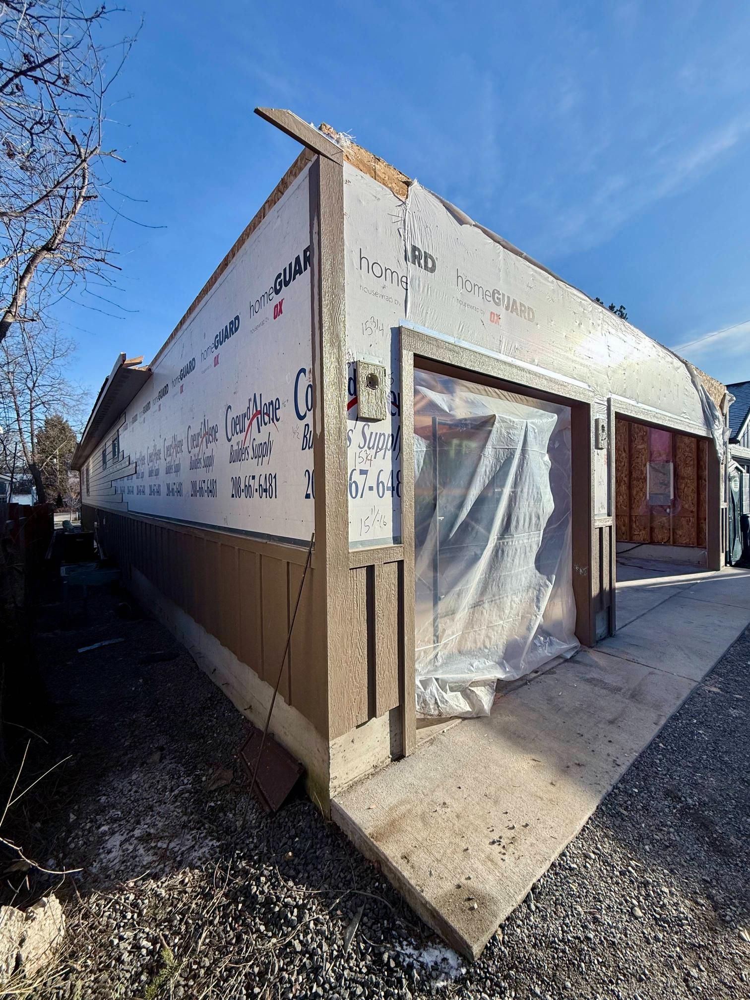 Building exterior under construction with exposed wood, siding, and doorway covered with plastic.