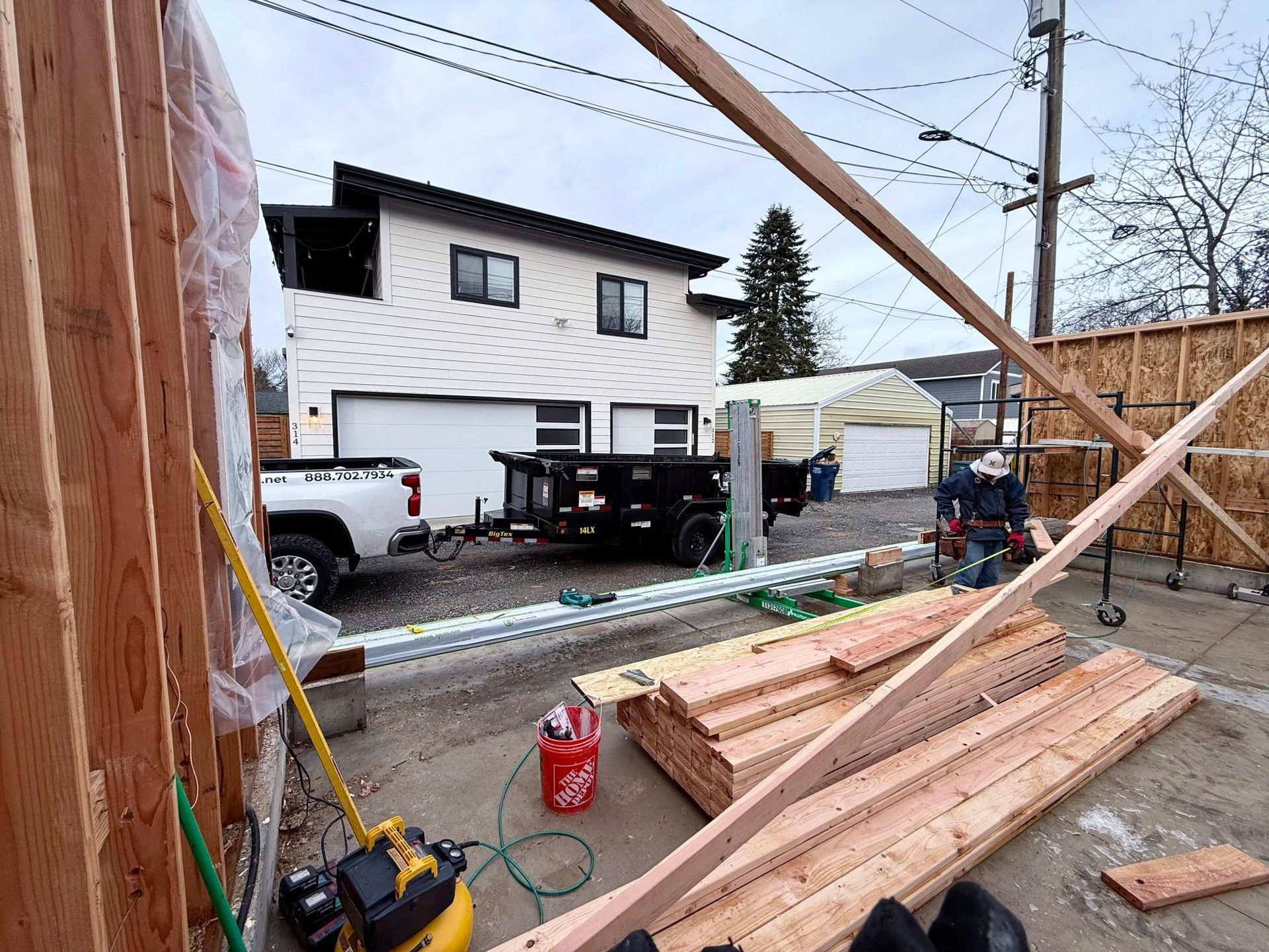 Construction site with house in background, wood framing, tools, truck and trailer.