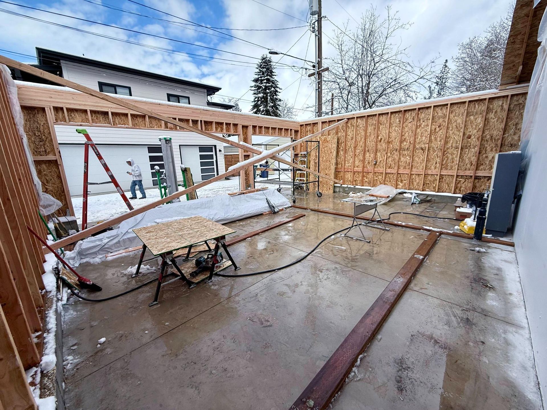 Construction of a wooden structure; snowy ground. Men in distance, tools and debris visible.