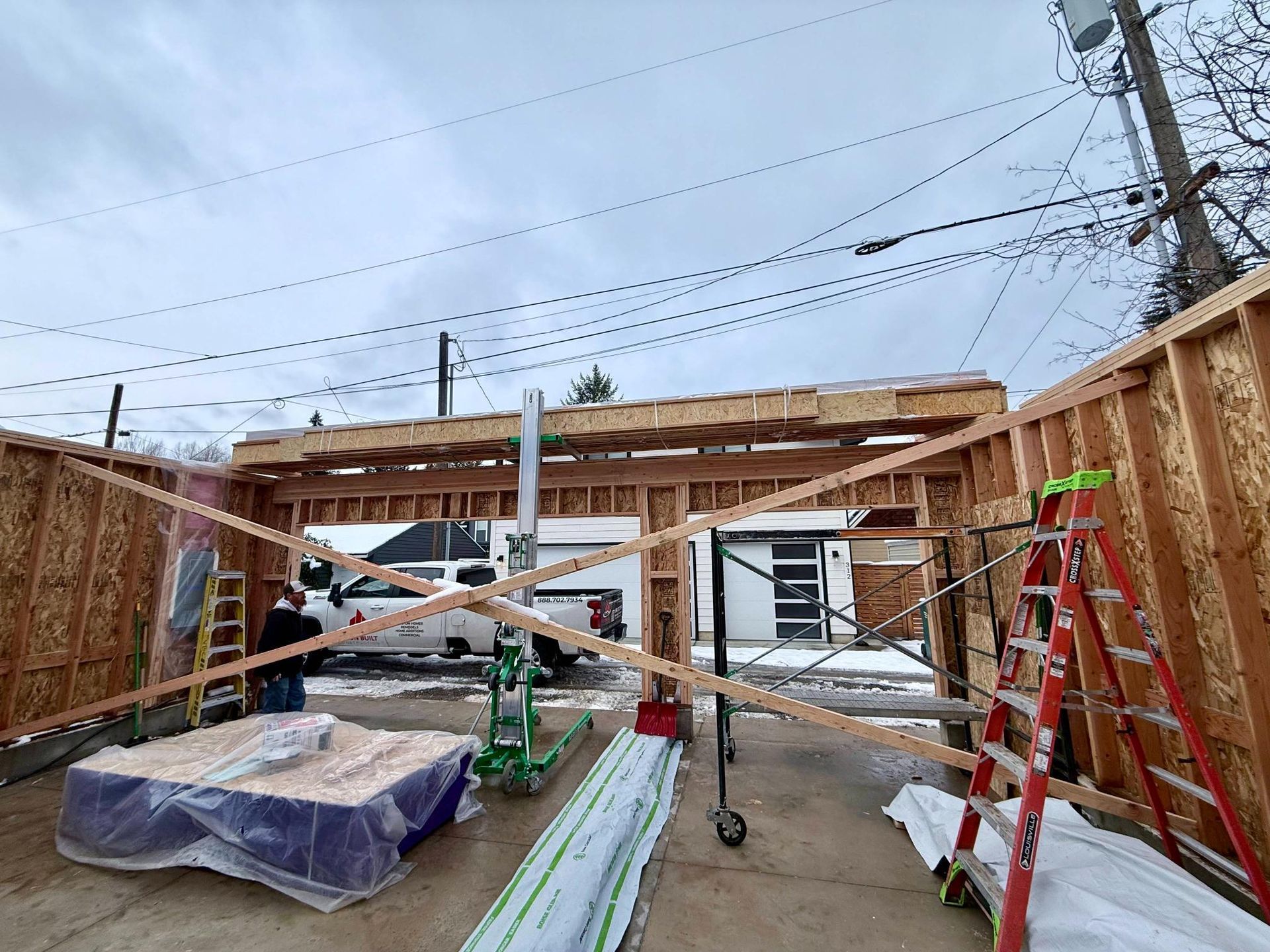 Garage under construction; wooden frame with cross bracing. Cloudy day, construction tools and materials visible.