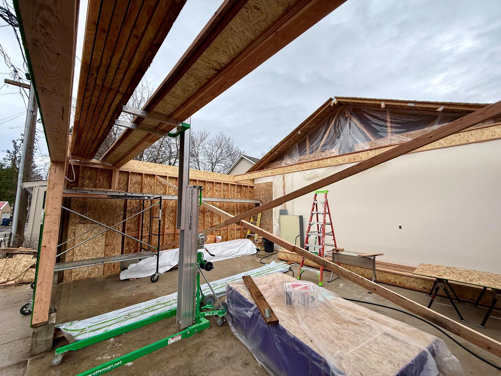 Construction site with exposed wooden framing. Scaffolding, lift, and materials present. Cloudy sky overhead.