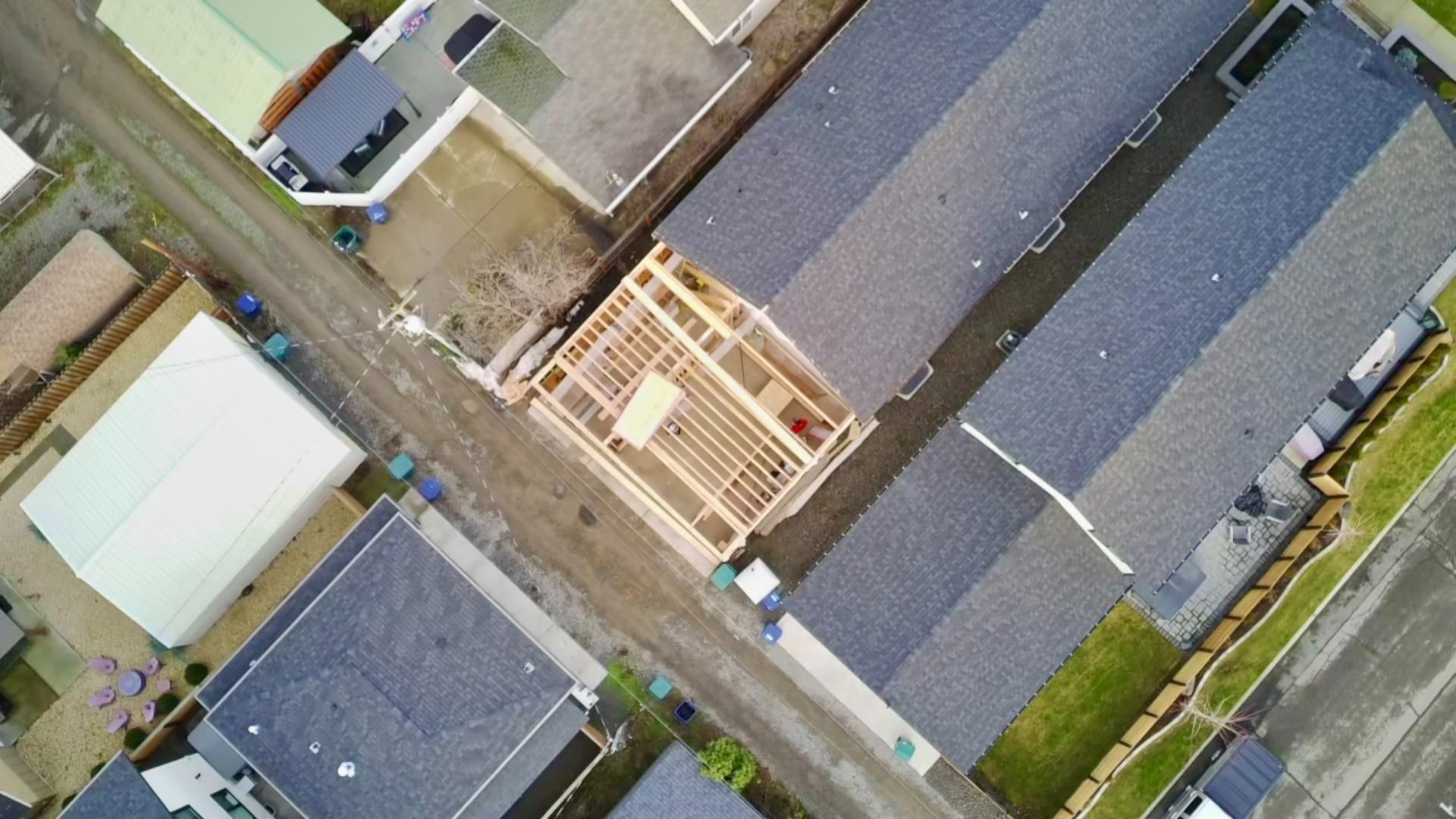 Aerial view of a house under construction surrounded by other houses with dark gray roofs.