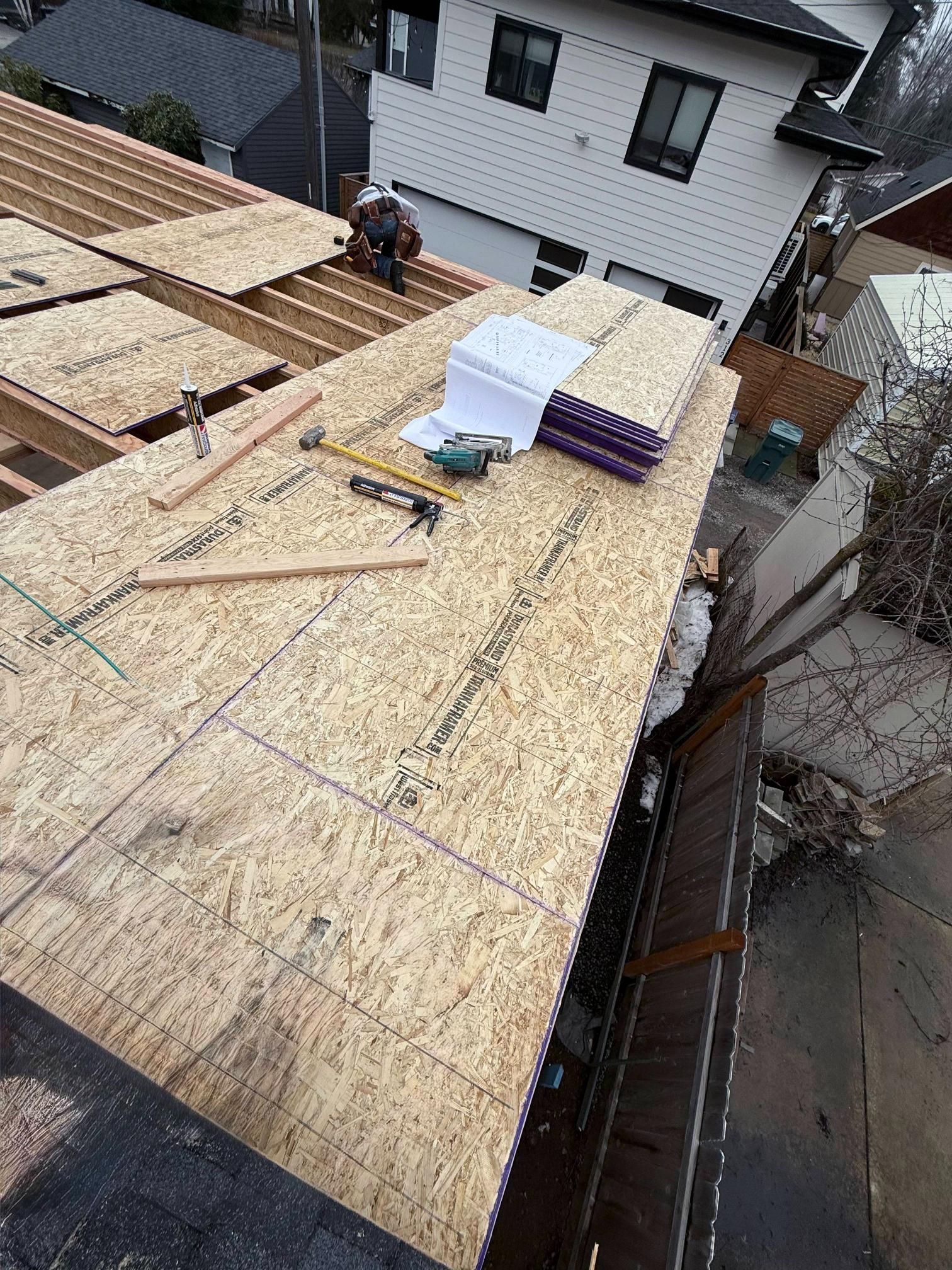 Construction worker on a roof installing OSB sheathing. House in background.
