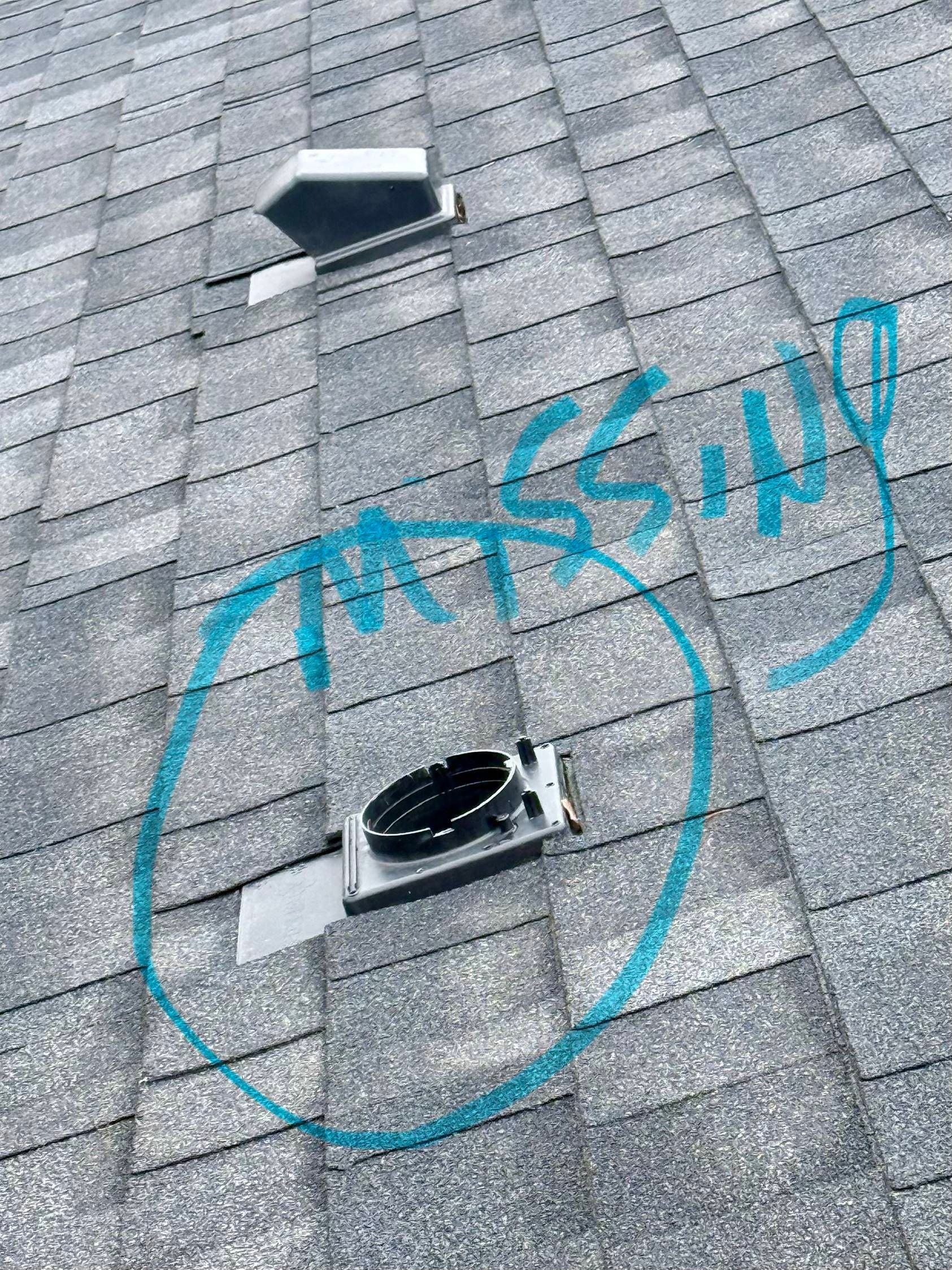 Gray shingle roof with two vents, a spray-painted blue circle, and text.