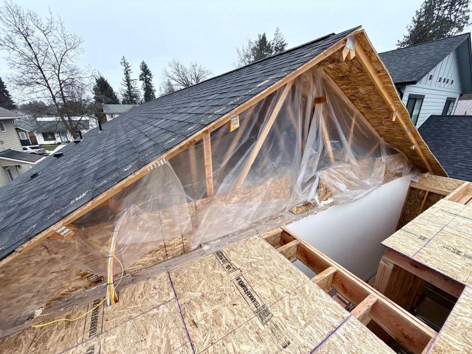 Roof under construction with exposed wooden beams, plywood, and protective plastic sheeting.