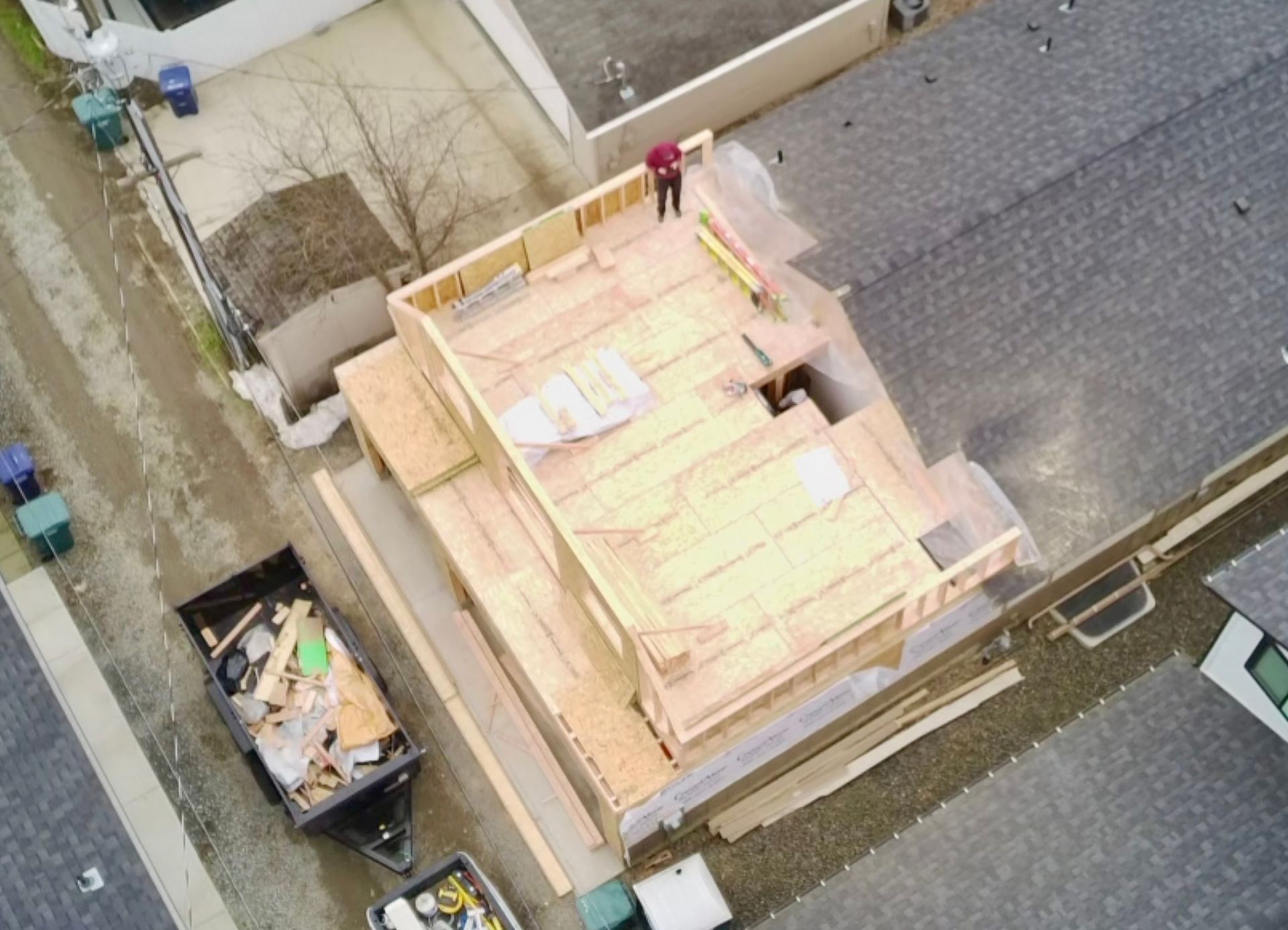 Aerial view of a building under construction. A person stands on the wooden frame rooftop.