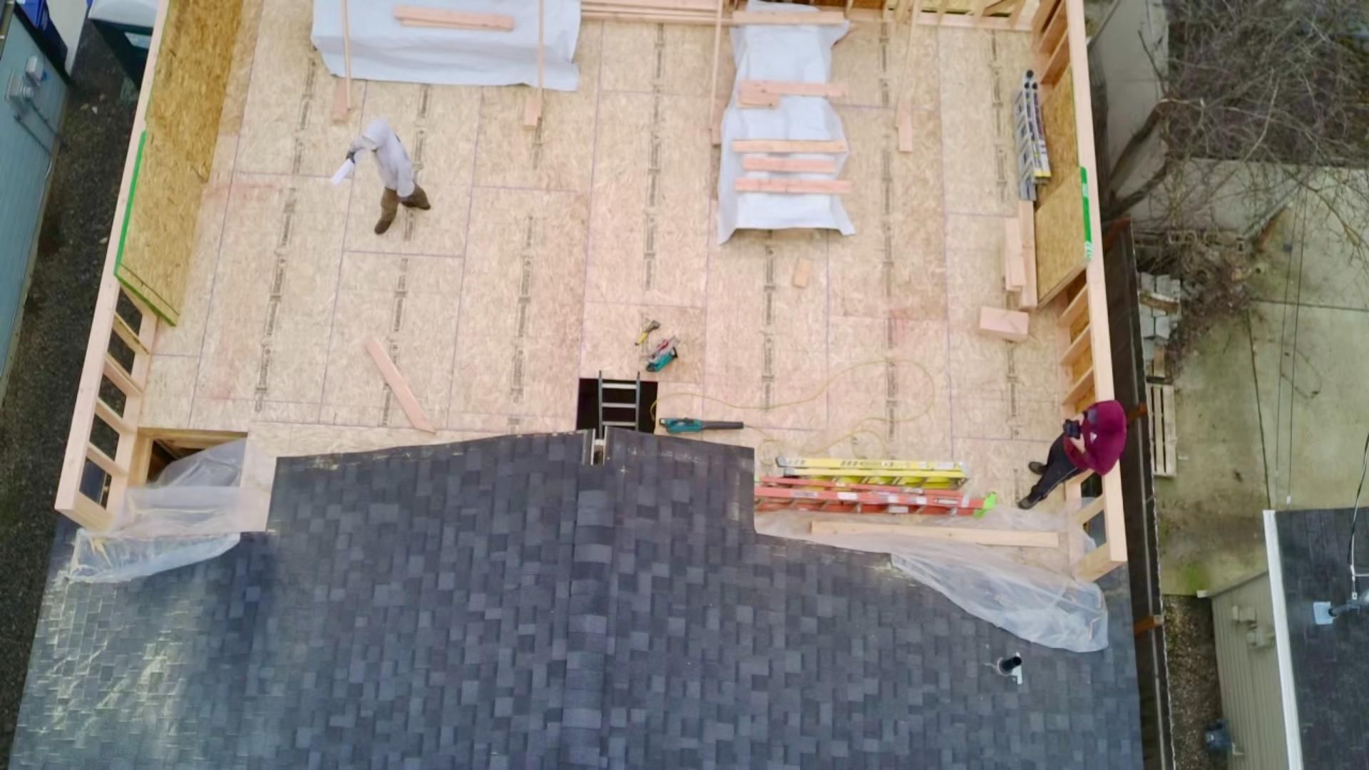 Construction of a building's frame. Roofers on a completed roof, workers inside, surrounded by lumber.