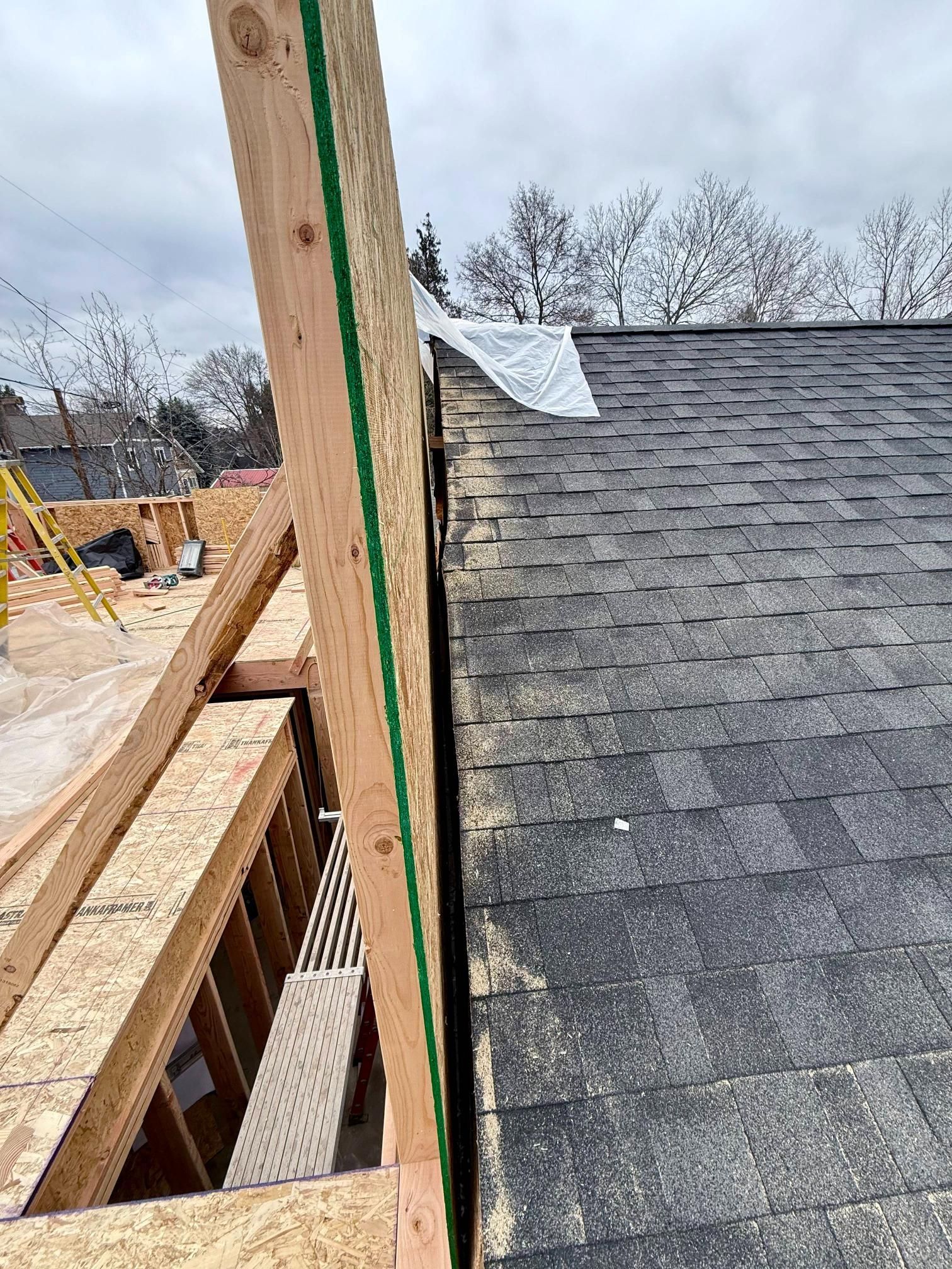 View of a roof with black shingles next to a wooden wall under construction.