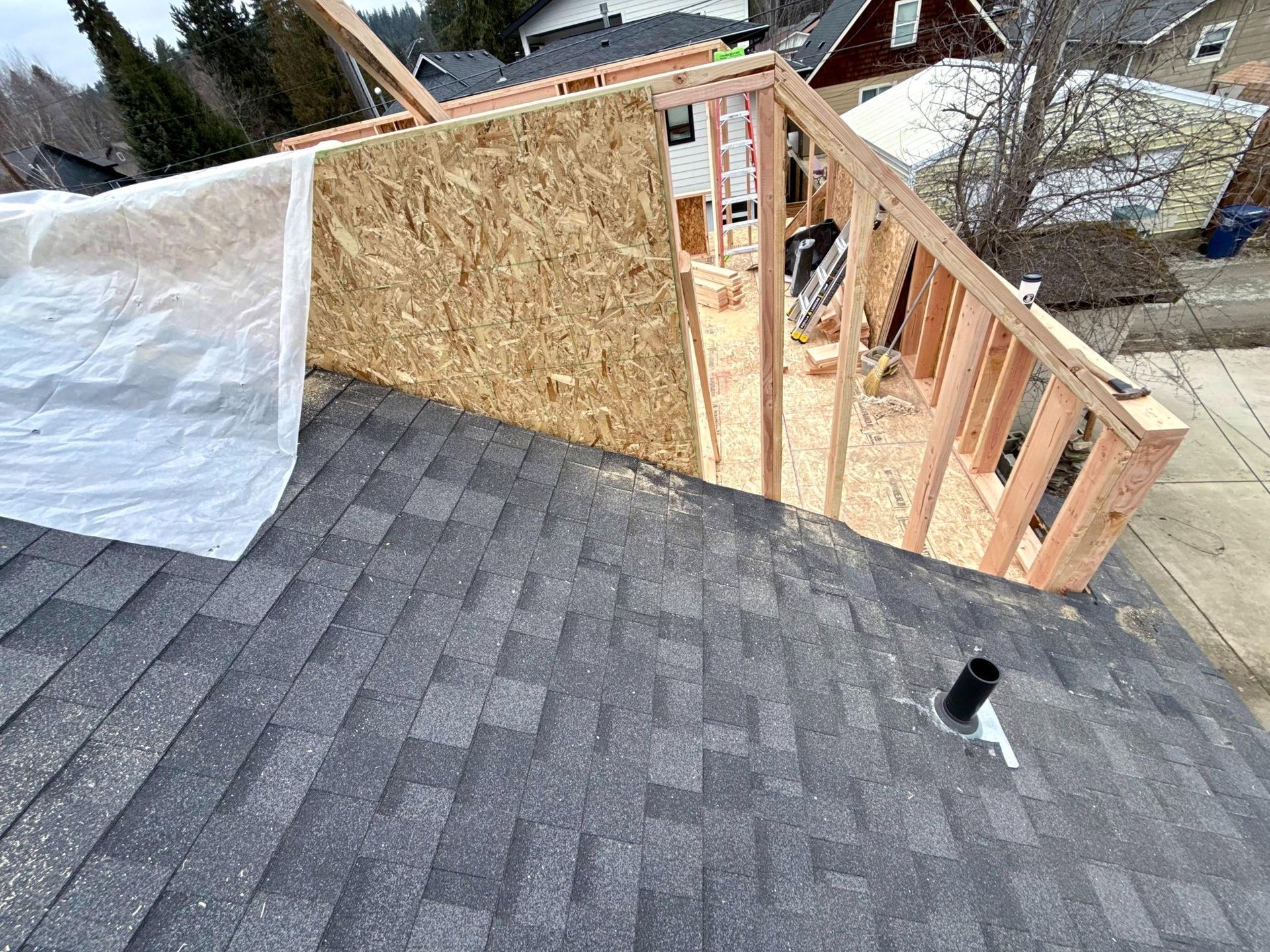 Rooftop construction: Framing and OSB board added to roof with asphalt shingles. Plastic sheet covers part.