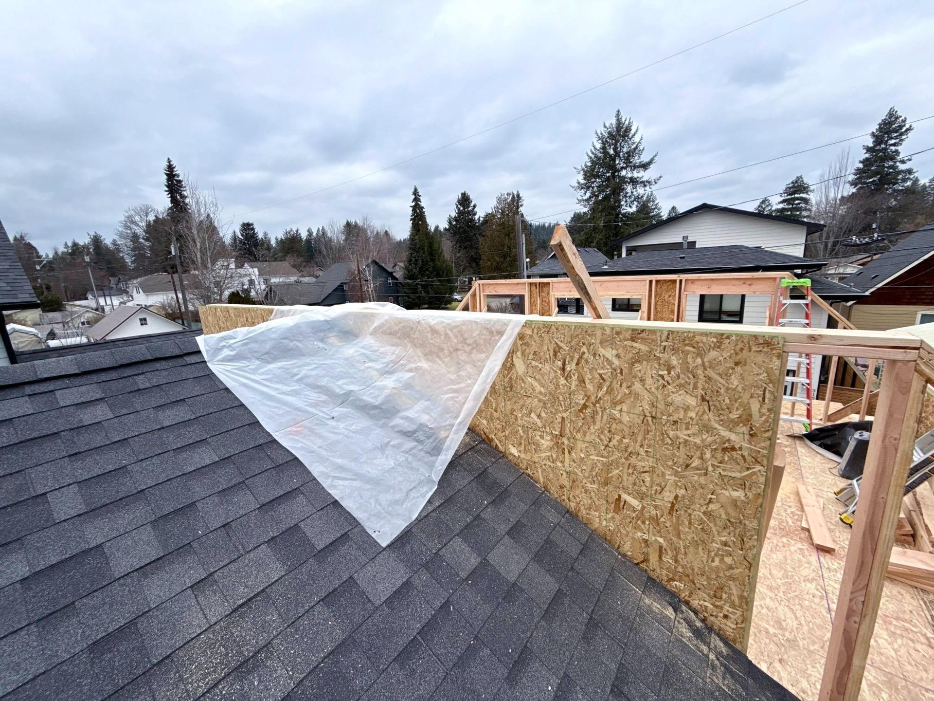 Construction site: Roof with tarp, unfinished walls, and surrounding houses under a cloudy sky.