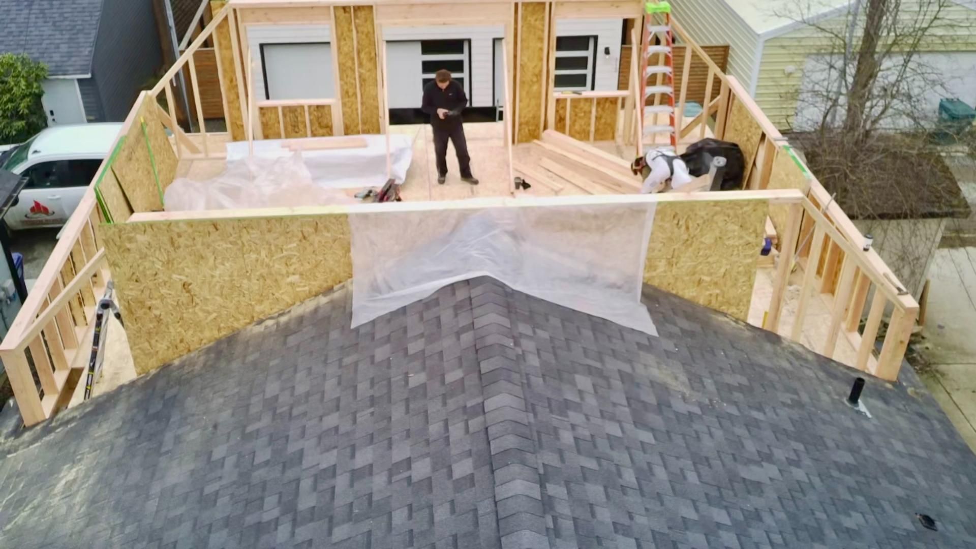 Construction of a home addition with wooden frame on a rooftop. A person and a dog are visible on the new deck.